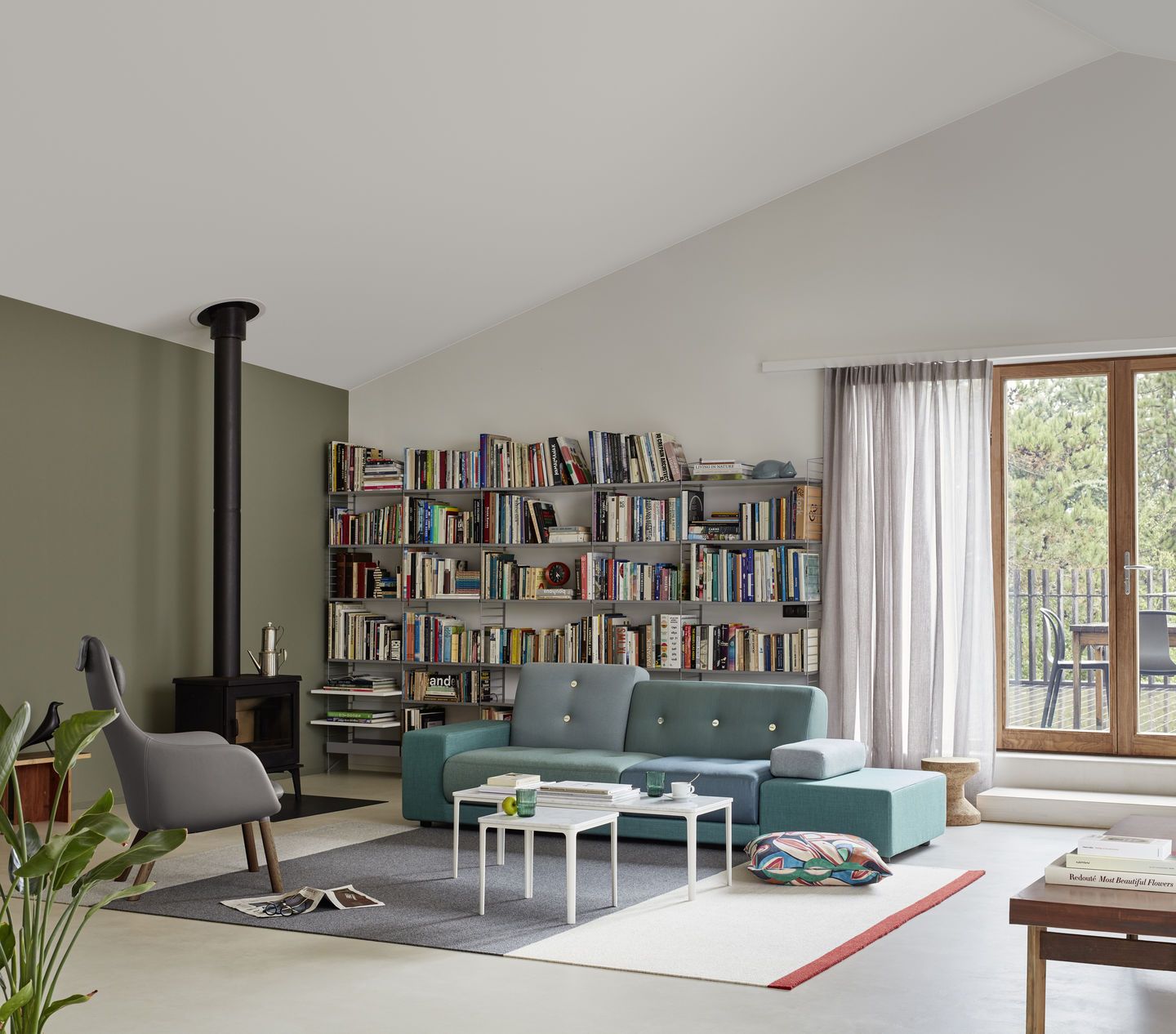Wohnzimmer mit blauem Polder Sofa von Vitra, Bücherregal und Kaminofen.