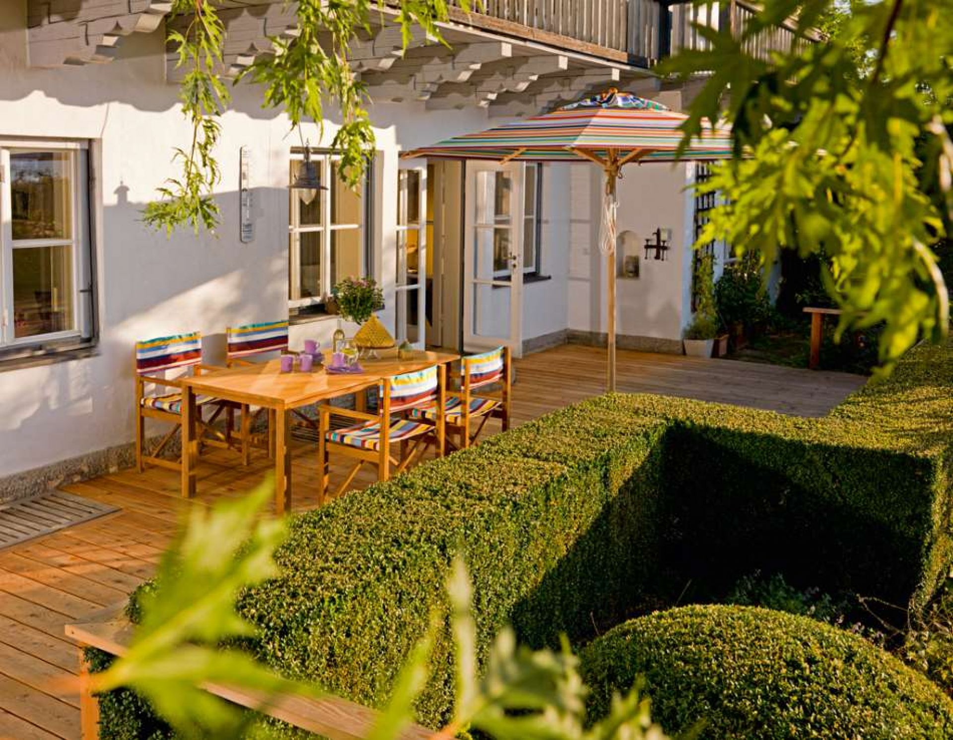Außenbereich mit Cabin Sessel Tanne von Weishäupl, Holztisch und Sonnenschirm auf Terrasse.