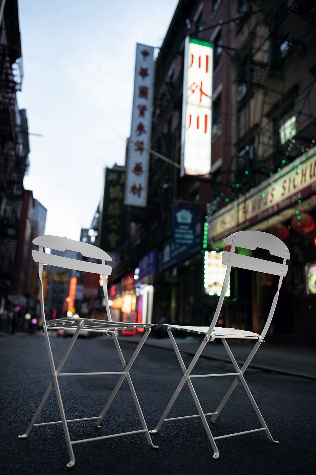 Zwei weiße La Môme Klappstühle von Fermob Outdoor auf einer Straße mit asiatischen Schriftzeichen im Hintergrund.