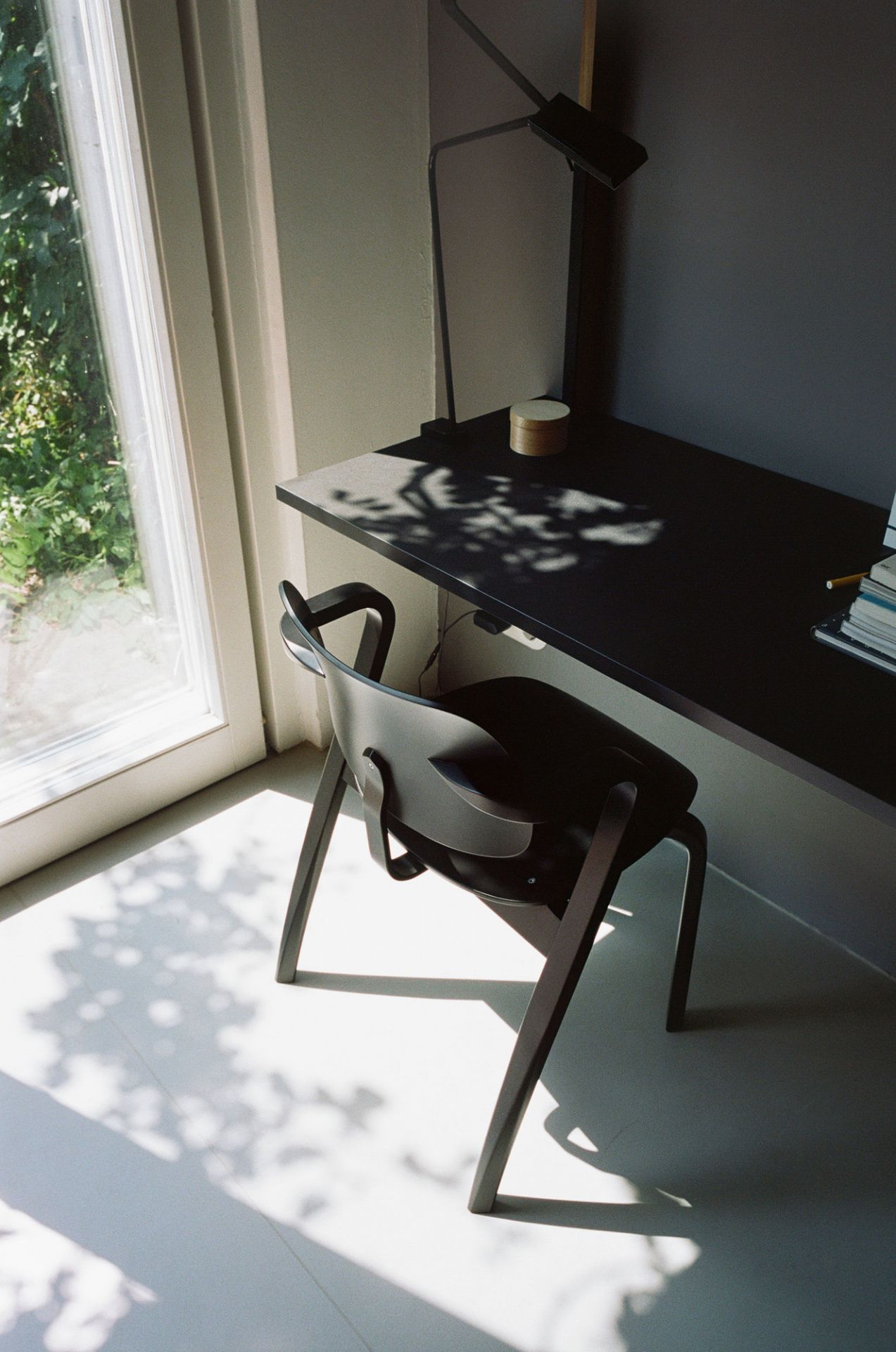 Schwarzer Aslak Chair Stuhl von Artek am Schreibtisch mit Lampe und Fenster im Hintergrund.