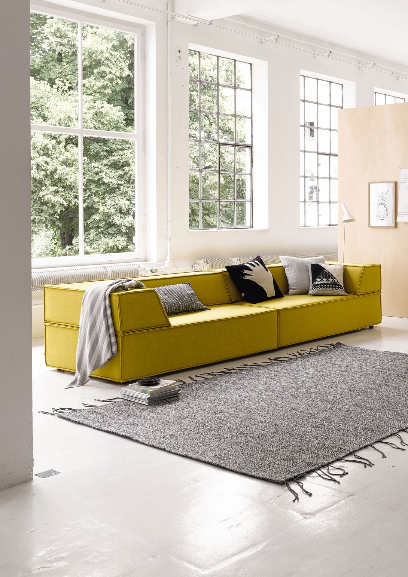 Gelbes Trio Modulsofa mit Kissen und Decke in modernem Wohnzimmer mit Teppich und großen Fenstern.