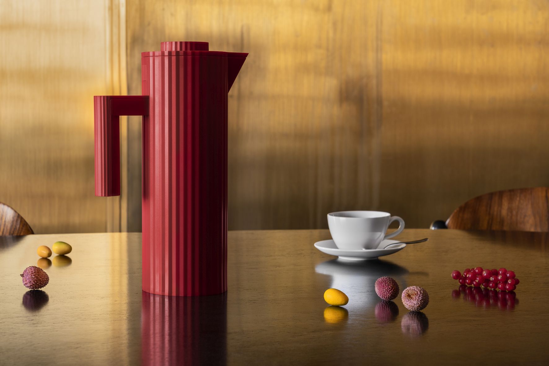 Rote Alessi Isolierkanne MDL12 mit Plissee-Design auf einem Tisch mit Tasse und Früchten.