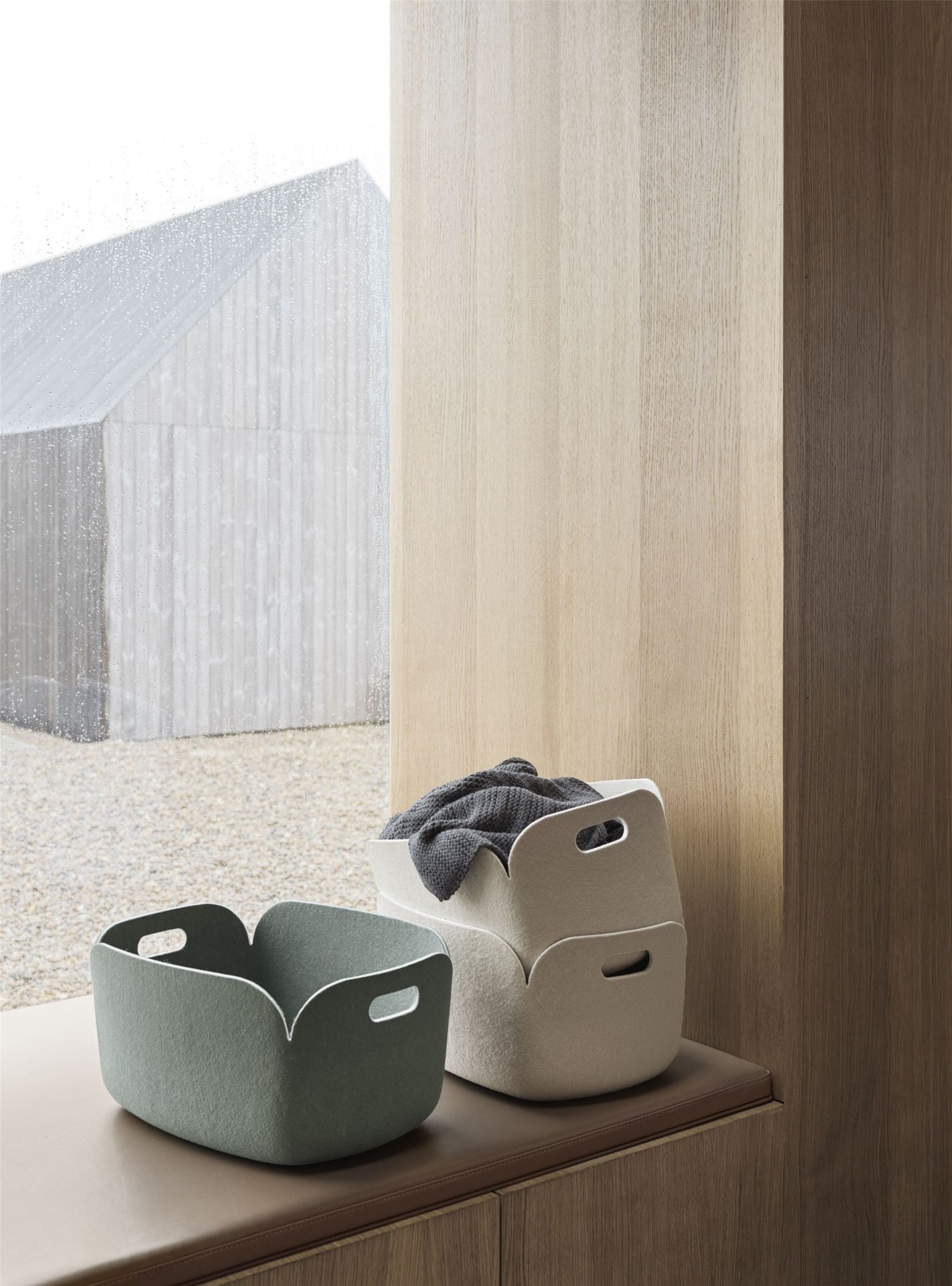 Zwei Muuto Restore Aufbewahrungskörbe: Staubgrün und Beige, einer mit Decke, auf Fensterbank.