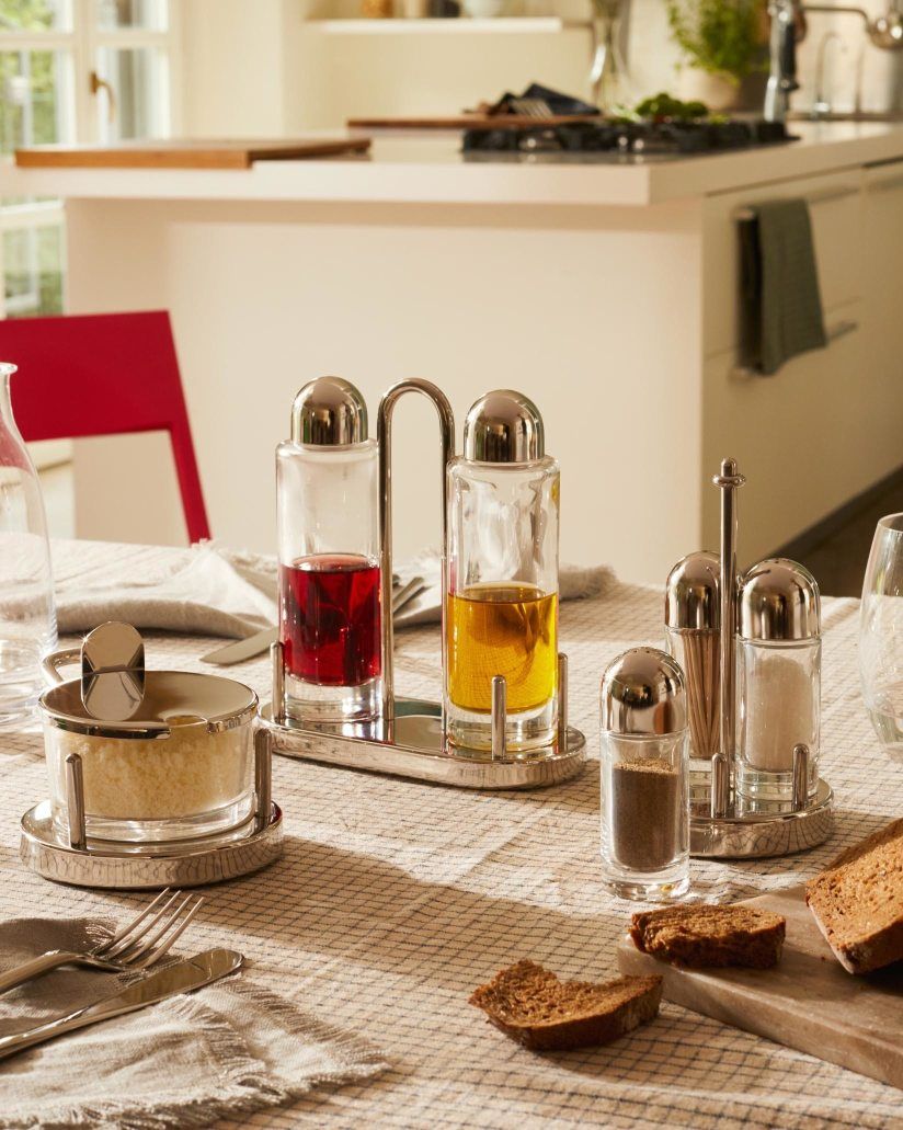 Alessi Käsedose 5071 und Gewürzständer-Set aus Edelstahl auf einem gedeckten Tisch, ideal für Küche und Esstisch.