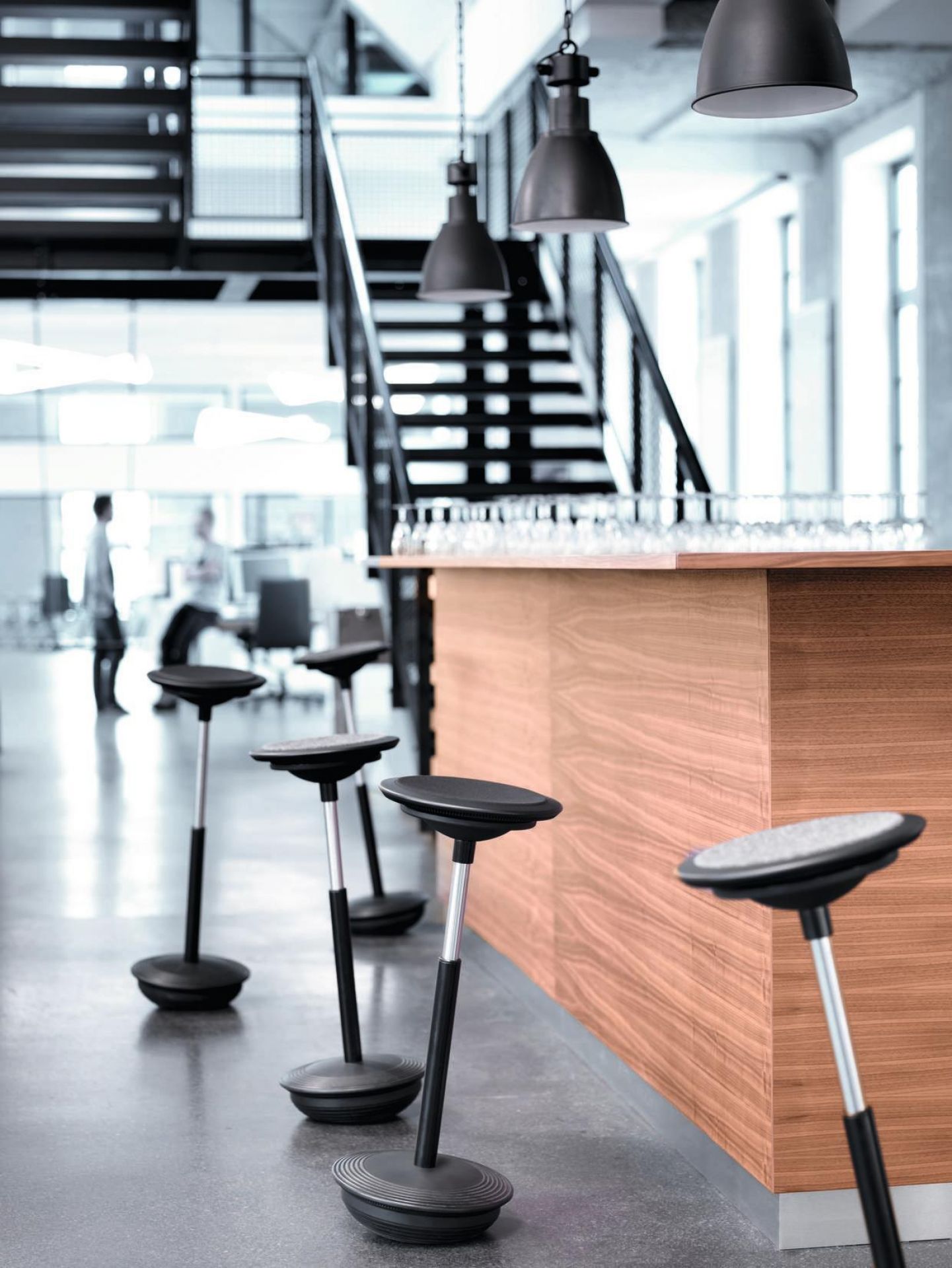 Stitz Stehhocker von Wilkhahn in einem modernen Büro mit Stehtisch und Treppe im Hintergrund.