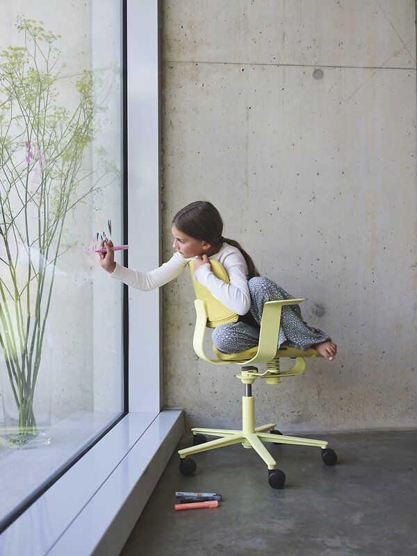 Mädchen malt auf Fenster, sitzend auf gelbem WiChair Drehstuhl von Wilkhahn, ergonomischer Bürostuhl.