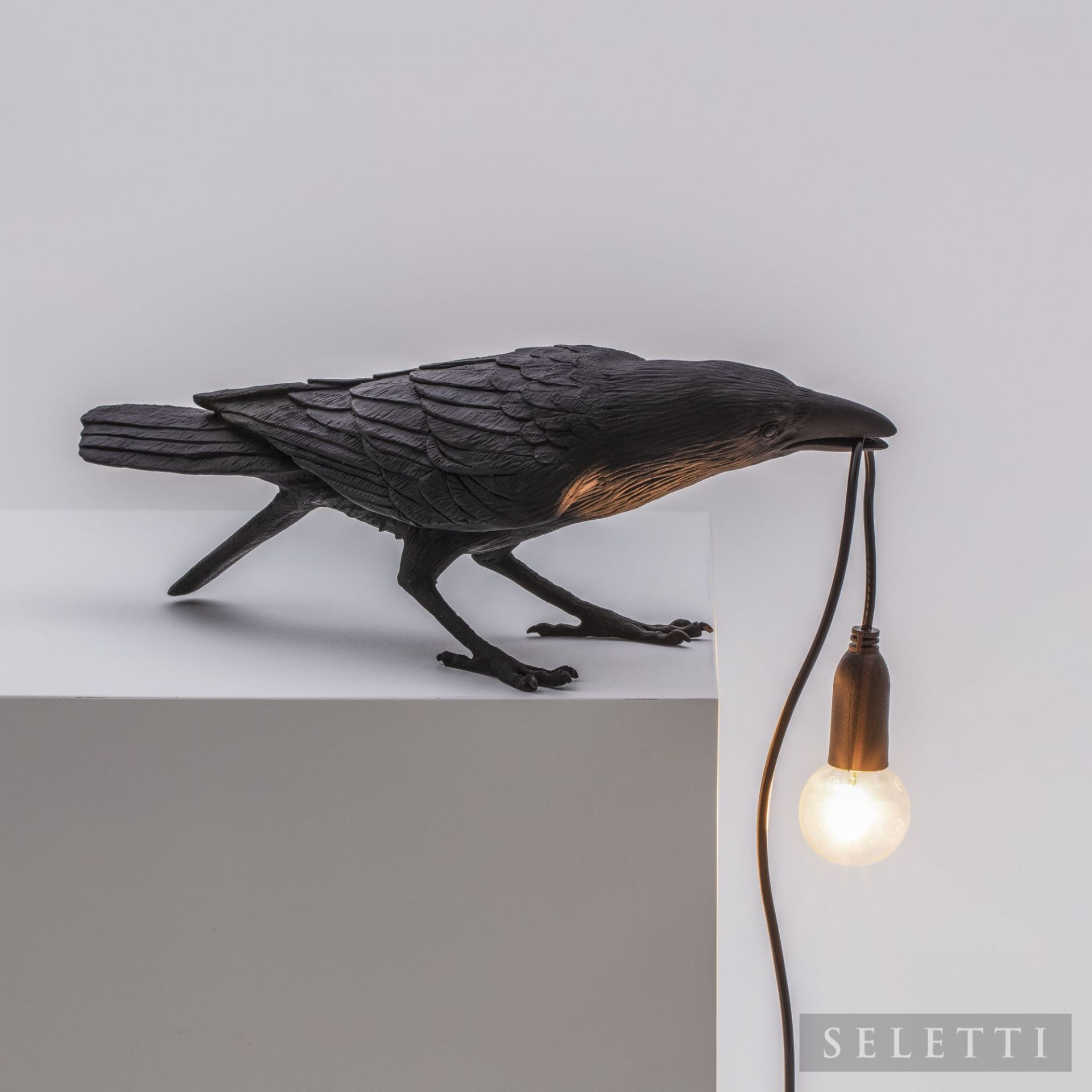 Schwarze Bird Lamp Playing von Seletti: Krähe hält mit dem Schnabel ein Kabel mit einer Glühbirne.