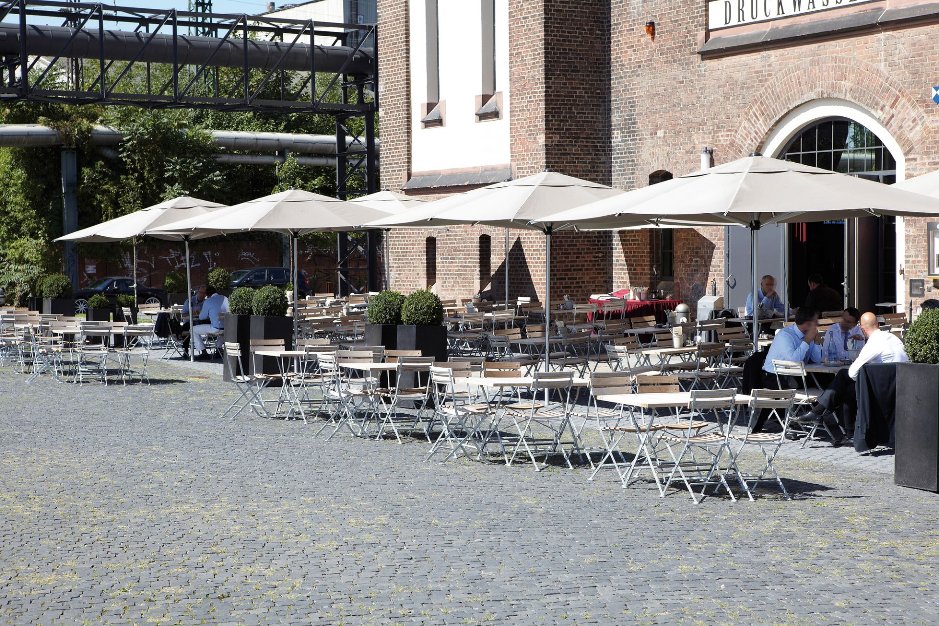 Außenbereich mit vielen Lucca Klapptischen in Natur von Jan Kurtz, ideal für Gastronomie.