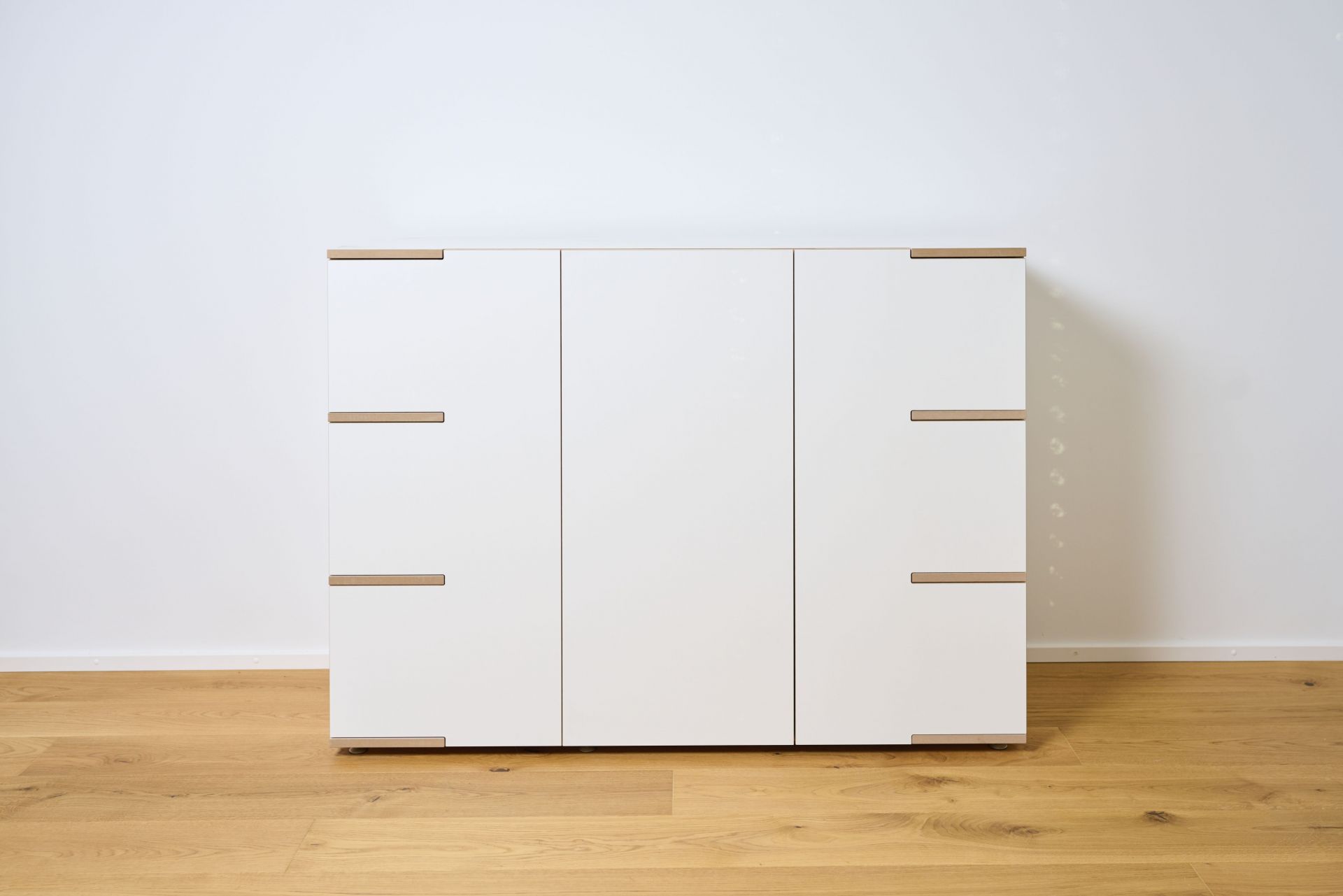 Tojo Stau Sideboard aus weißem Holz mit drei Türen und Griffen auf hellem Holzboden.