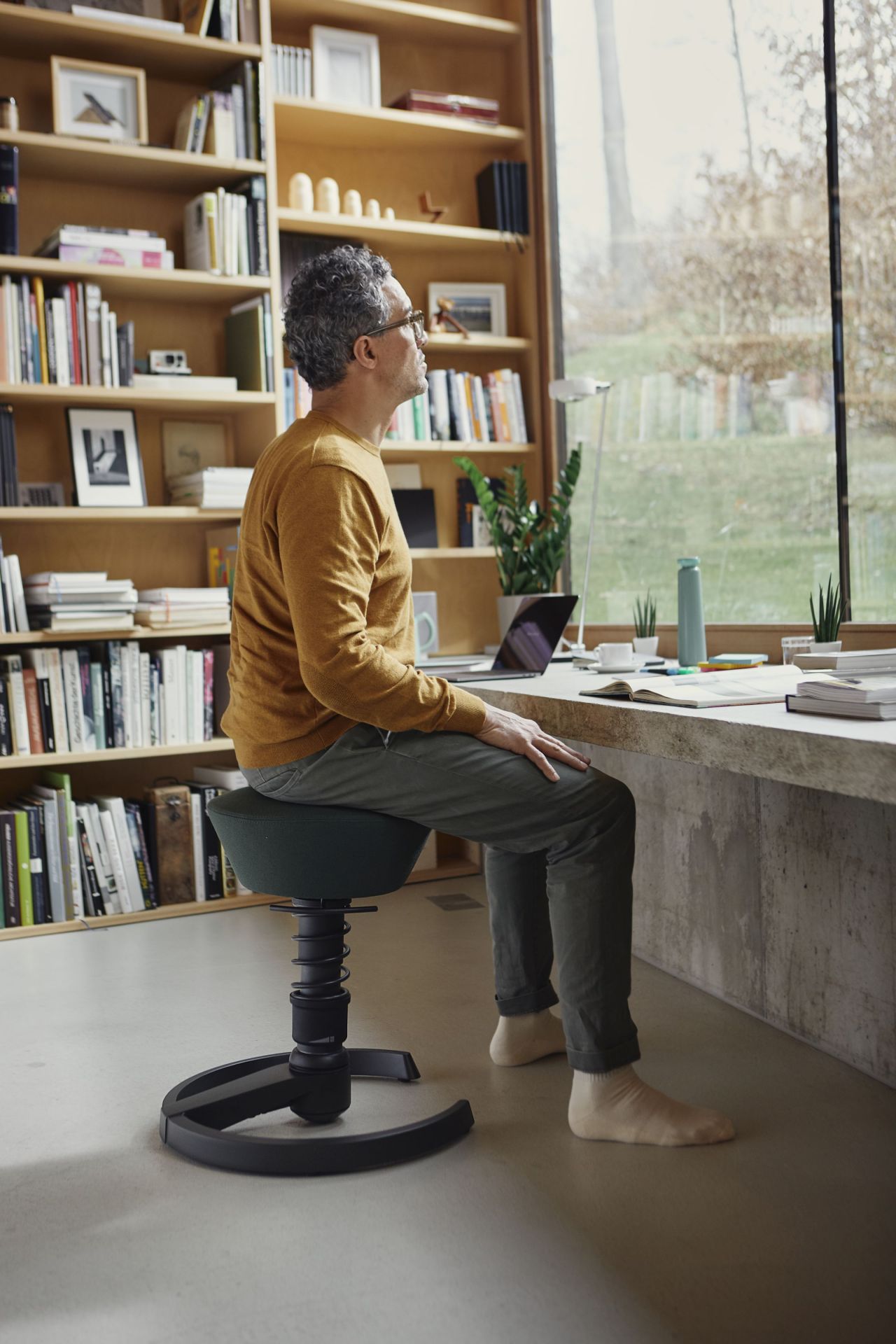 Mann sitzt auf ergonomischem Swopper Bürostuhl in Grün, konzentriert am Schreibtisch mit Laptop und Blick nach draußen.
