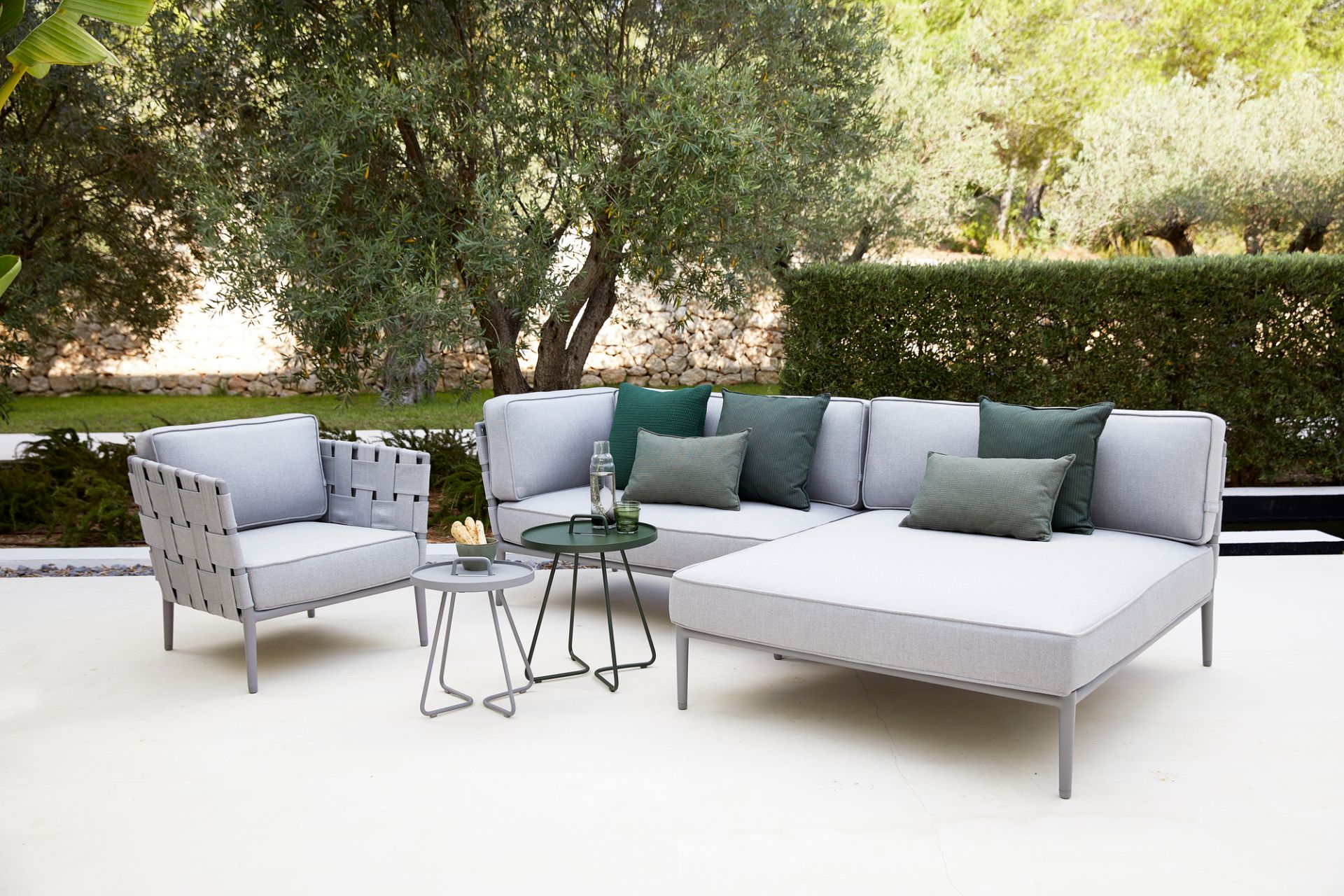 Conic AirTouch Outdoor Modulsofa hellgrau von Cane-Line mit Sessel und Beistelltischen im Garten.