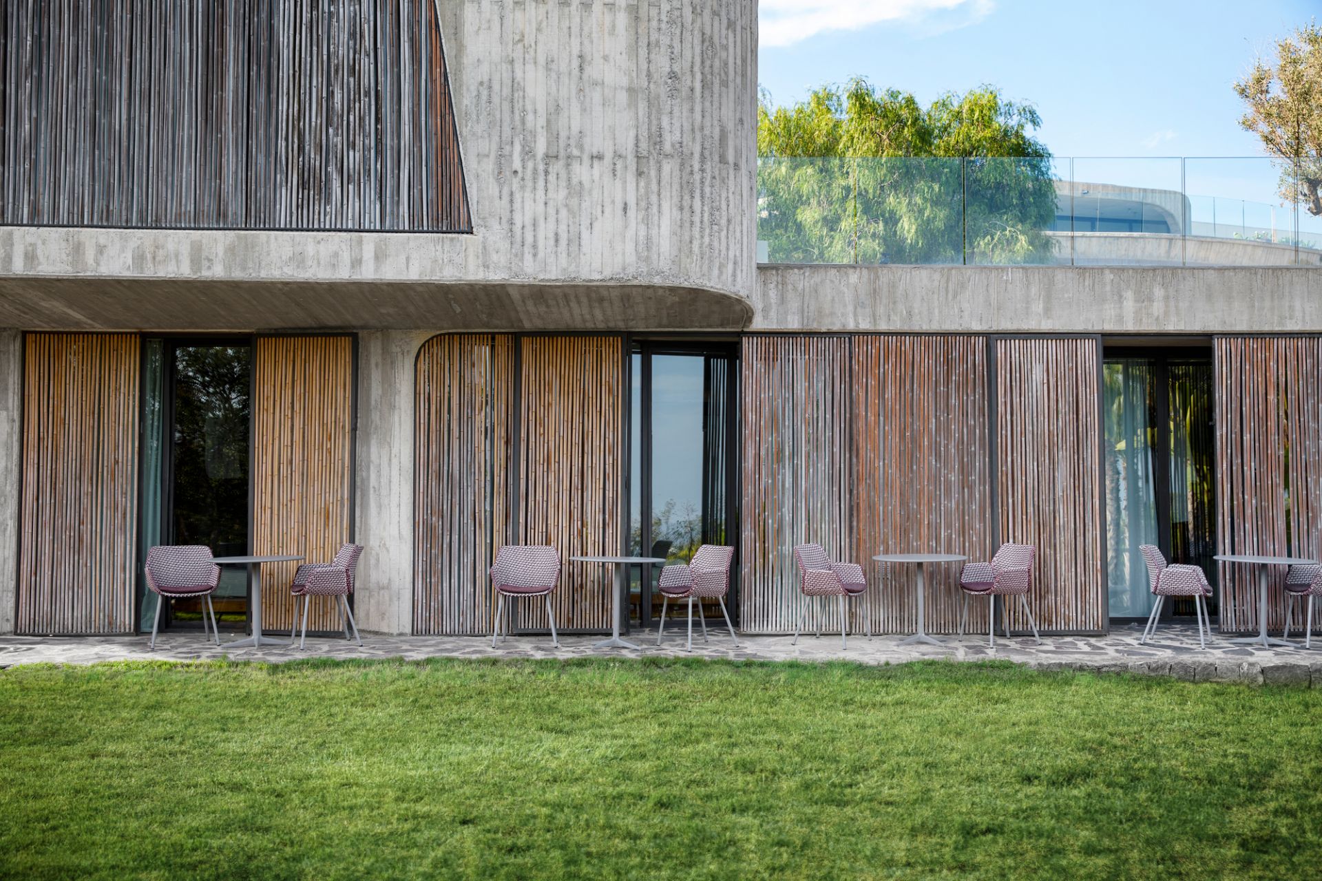 Cane-Line Vibe Outdoor Sessel vor modernem Gebäude mit Bambusverkleidung und gepflegtem Rasen.