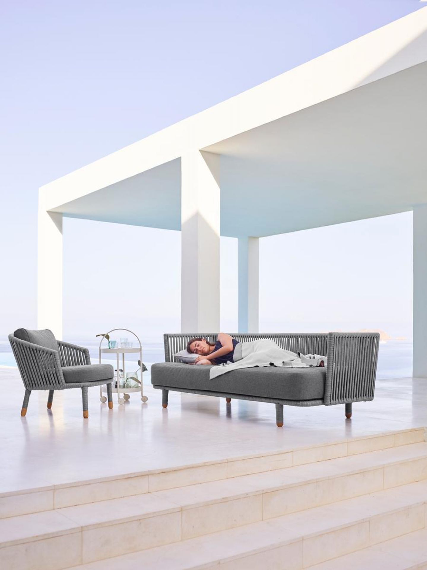 Frau entspannt auf Cane-Line Moments Outdoor Lounge Sofa und Sessel, graue Gartenmöbel mit Seilgeflecht.