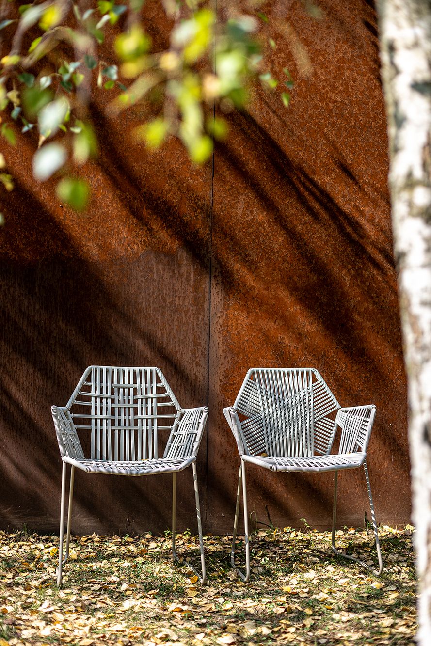 Zwei Tropicalia Armlehnstühle von Moroso im Freien vor einer rostfarbenen Wand, Outdoor Möbel.