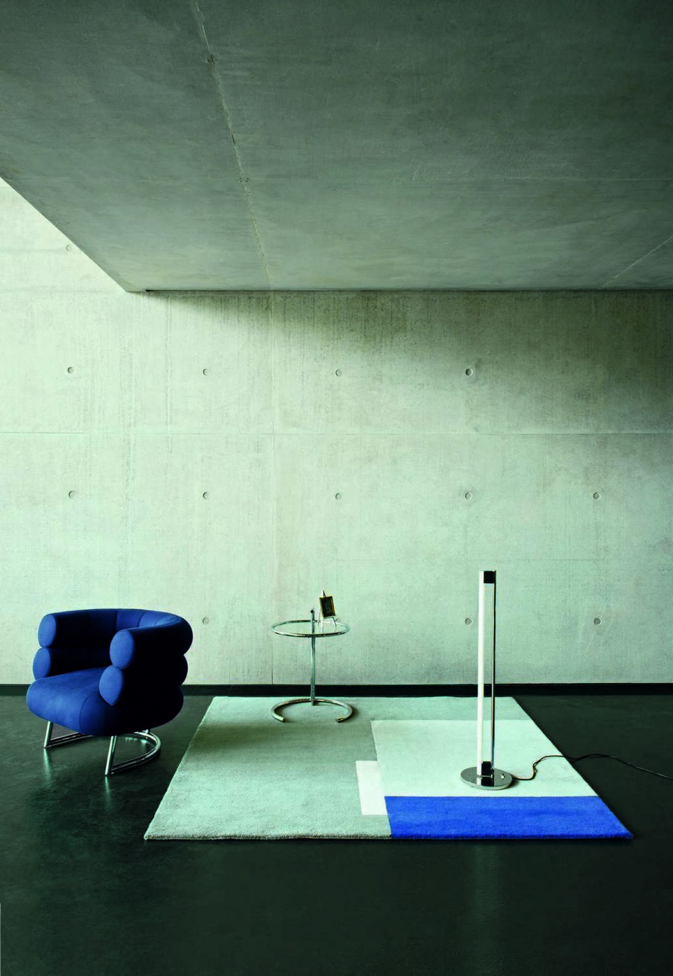 Minimalistisches Interieur mit ClassiCon Tube Light Stehleuchte in Schwarz, blauer Sessel und Glastisch.
