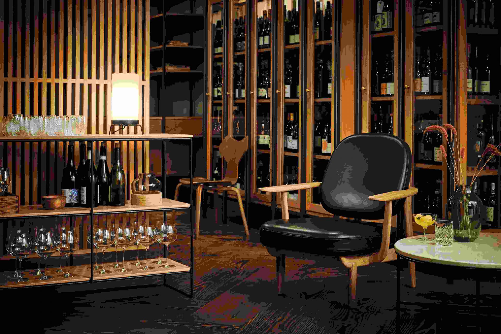 Schwarzer Grand Prix Stuhl von Fritz Hansen mit Holzgestell in einer Bar mit Weinregalen.