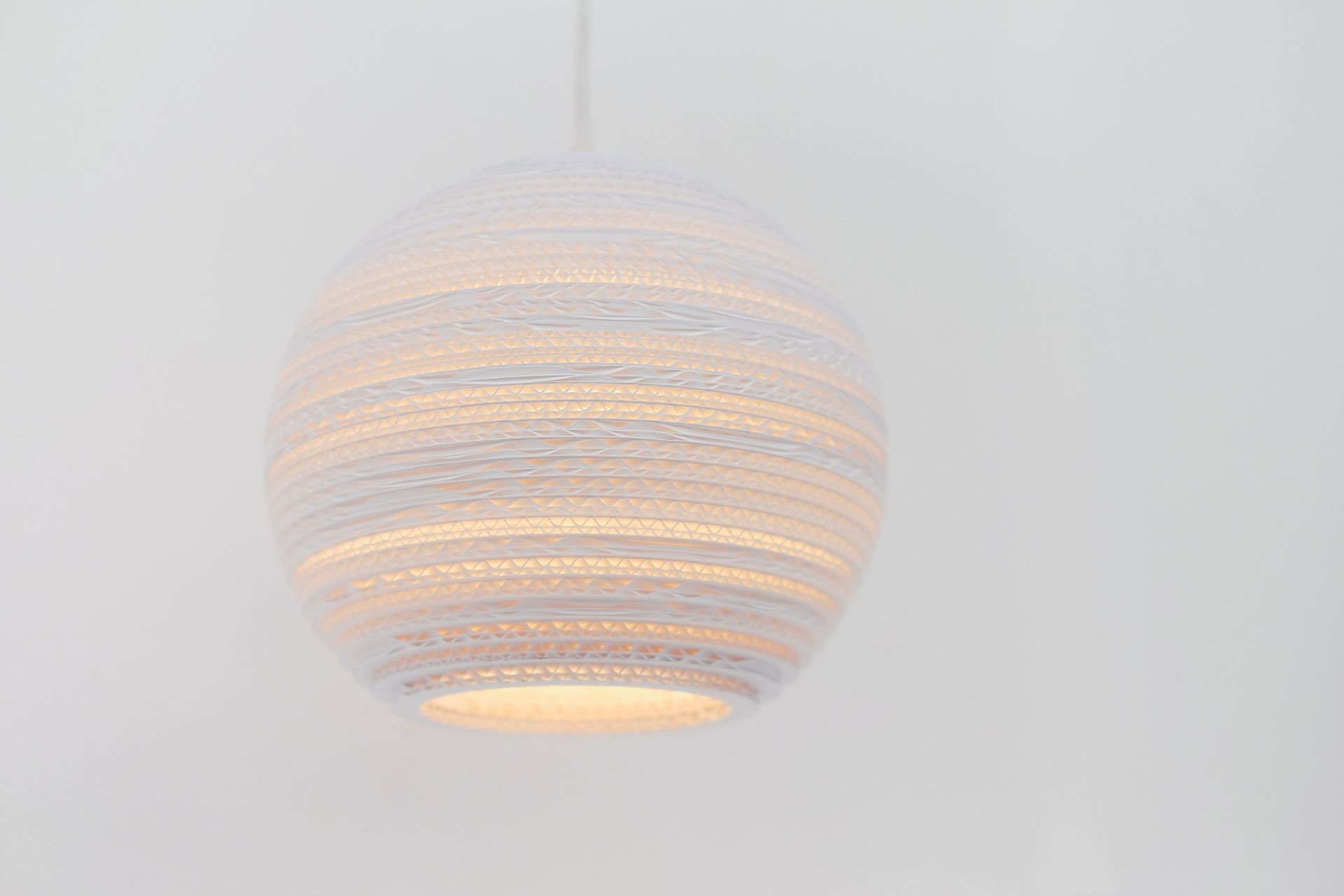 Weiße Scraplights Moon Hängeleuchte von Graypants aus recycelter Pappe, warmes Licht scheint durch die Lamellen.