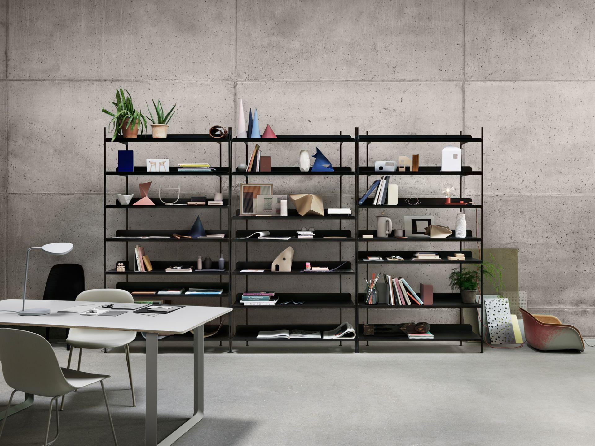 Schwarzes Compile Regalsystem von Muuto vor einer Betonwand, dekoriert mit Büchern und Deko-Objekten.