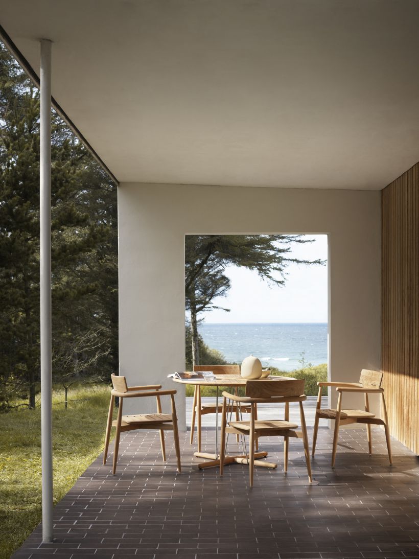 E022 Embrace Outdoor Tisch von Carl Hansen & Søn mit Stühlen auf Terrasse mit Meerblick.