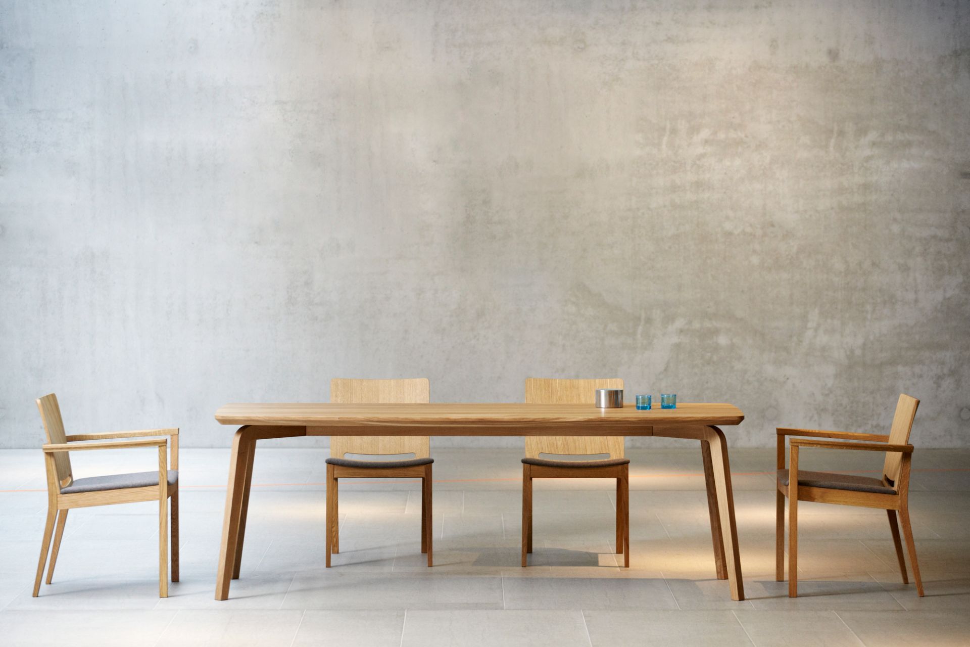 Kelley Armlehnstuhl von Jan Kurtz aus Holz mit grauem Sitzkissen am Esstisch.