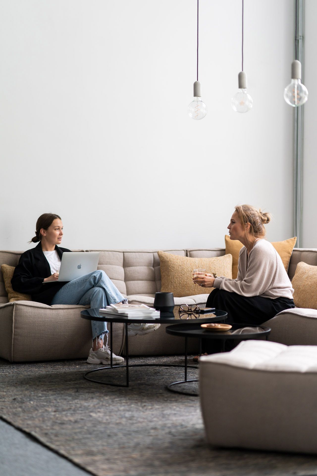 Zwei Frauen sitzen auf einem Sofa mit Ethnicraft Kissen in Sandfarbe und unterhalten sich.