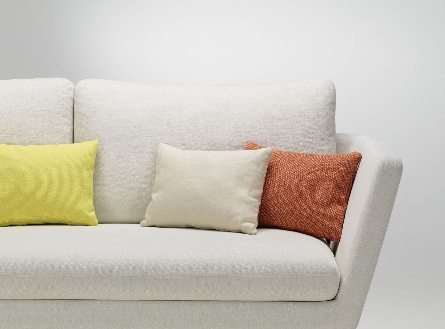 Nahaufnahme von drei Vitra Kissen in Gelb, Beige und Orange auf einem weißen Sofa.
