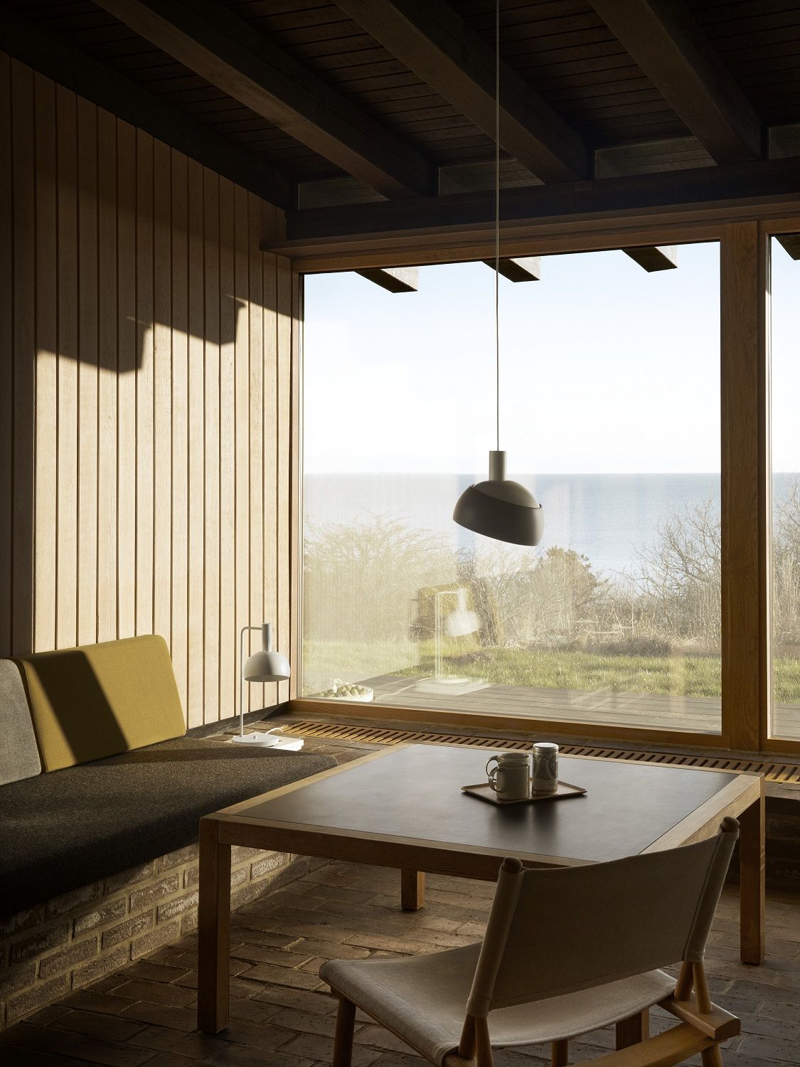FJ Elements Pendelleuchte von Louis Poulsen über Esstisch in modernem, hellen Wohnraum mit Meerblick.