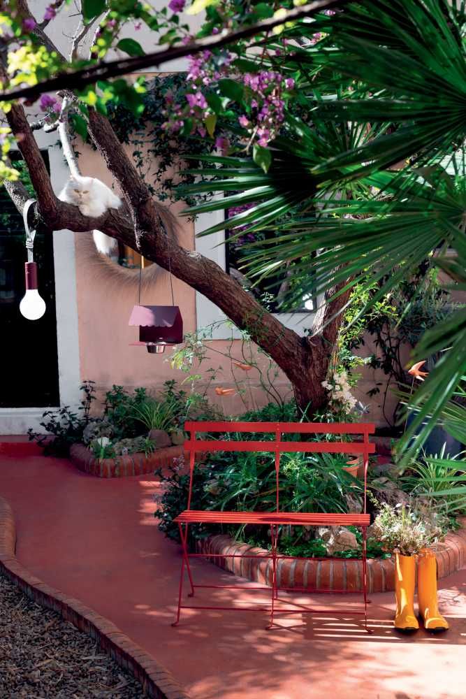 Rote Fermob Bistro Klappbank für zwei Personen im Garten mit Pflanzen und Dekoration.