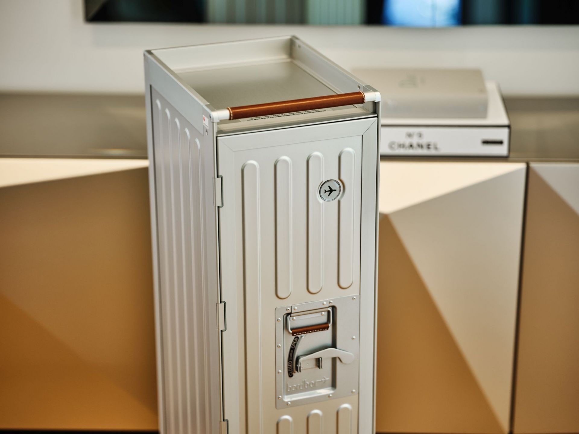 Silberner Voyager Flugzeugtrolley Bordbar mit braunem Griff vor modernem Sideboard, ideal als Designmöbel und Hausbar.