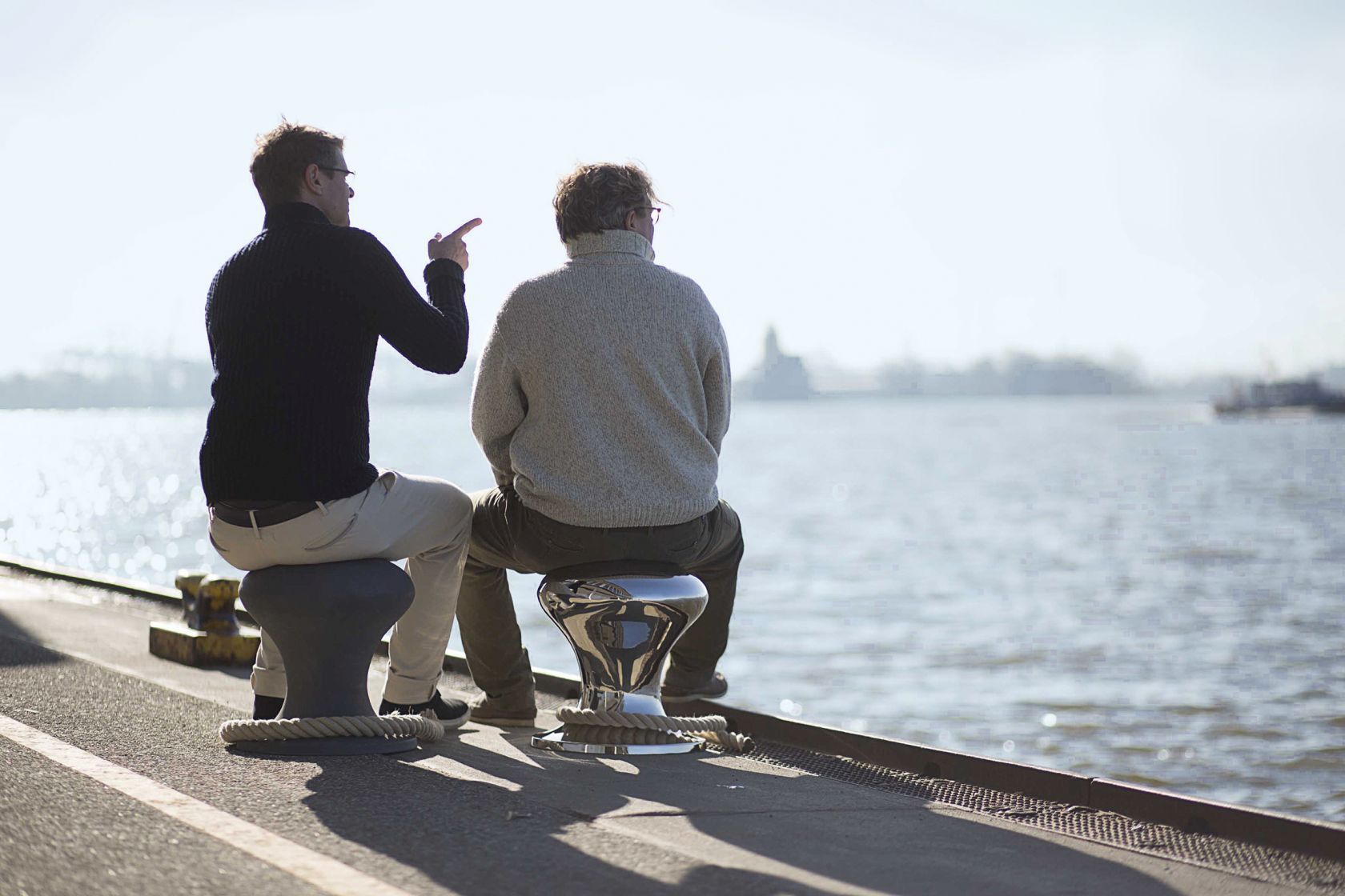 Zwei Männer sitzen auf dem Hamburger Hocker von Philippi am Hafen und schauen aufs Wasser.