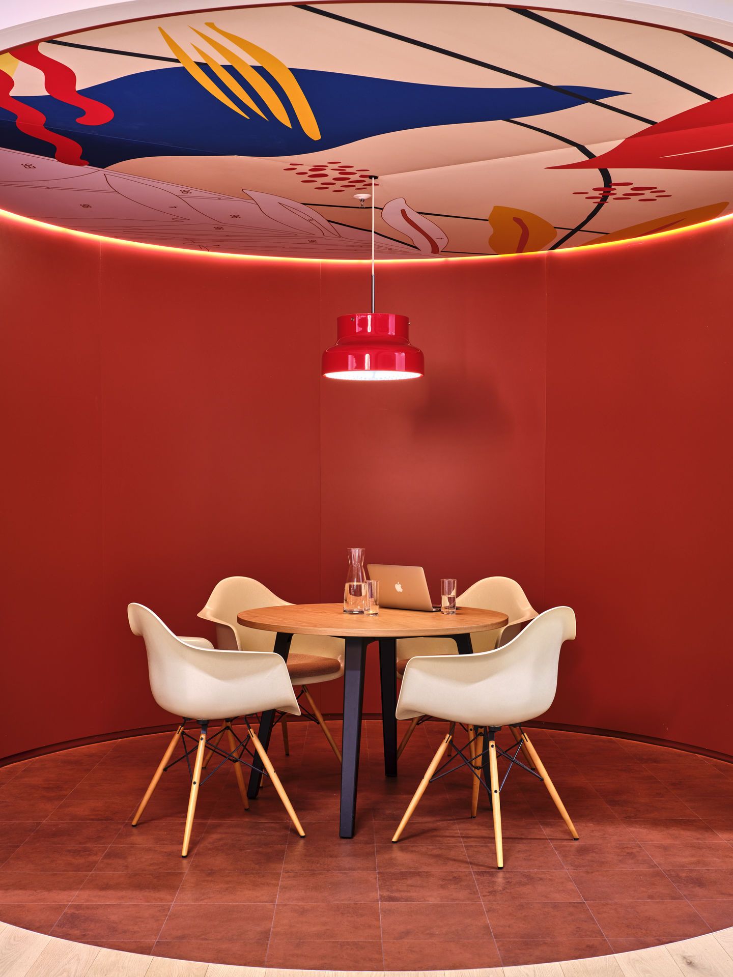 Innenraum mit vier hellen Eames Plastic Arm Chairs DAW Stühlen um einen runden Tisch.