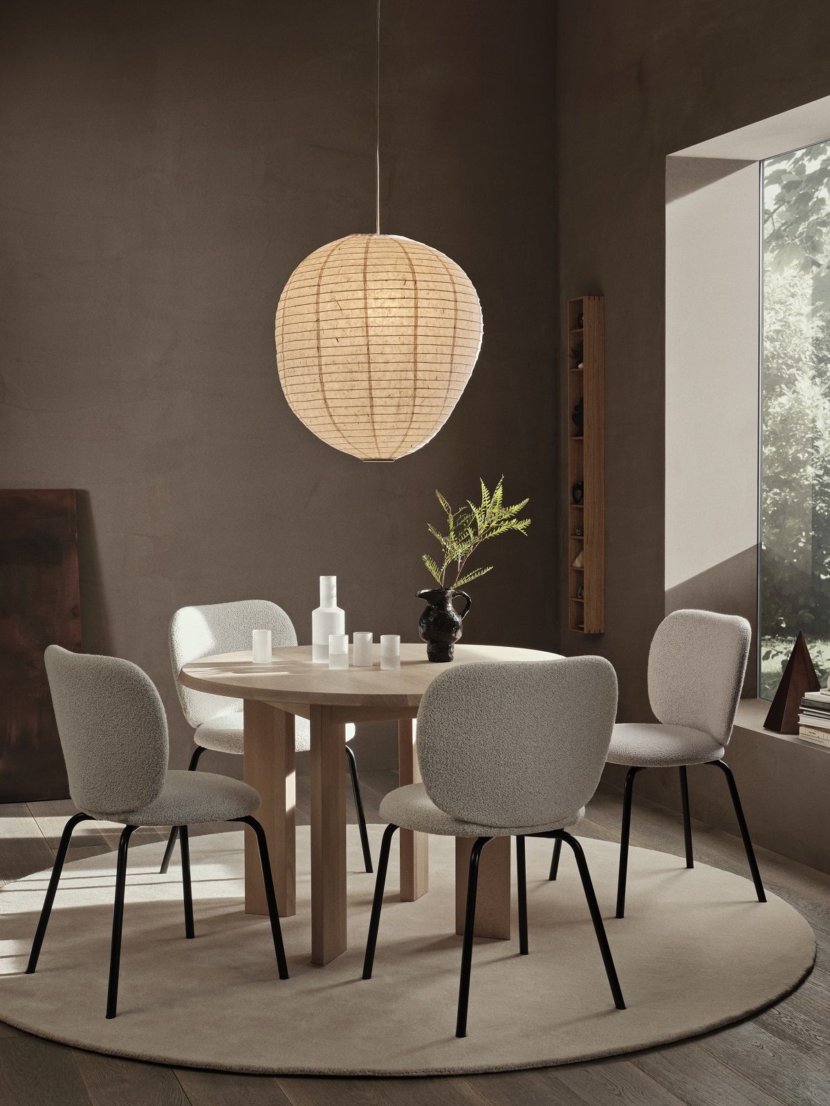 Esszimmer mit rundem Ferm Living Esstisch Tarn, Stühlen, Pendelleuchte und Dekoration auf beigem Teppich.