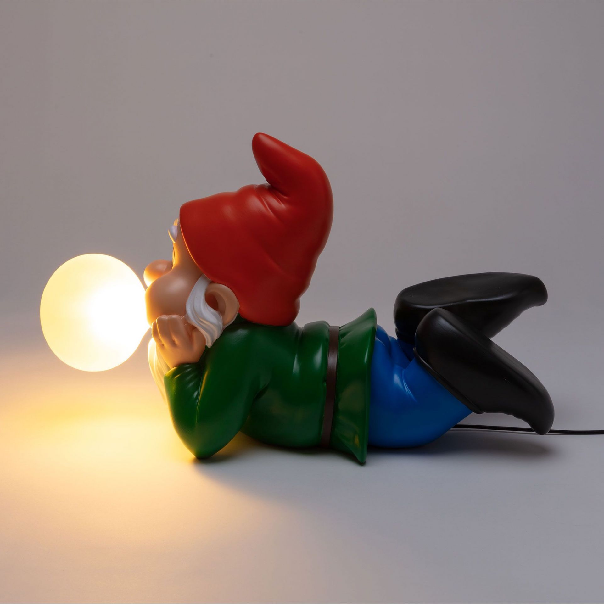 Gummy Dreaming Leuchte von Seletti: Liegender Gartenzwerg mit roter Mütze, der eine leuchtende Kugel hält.