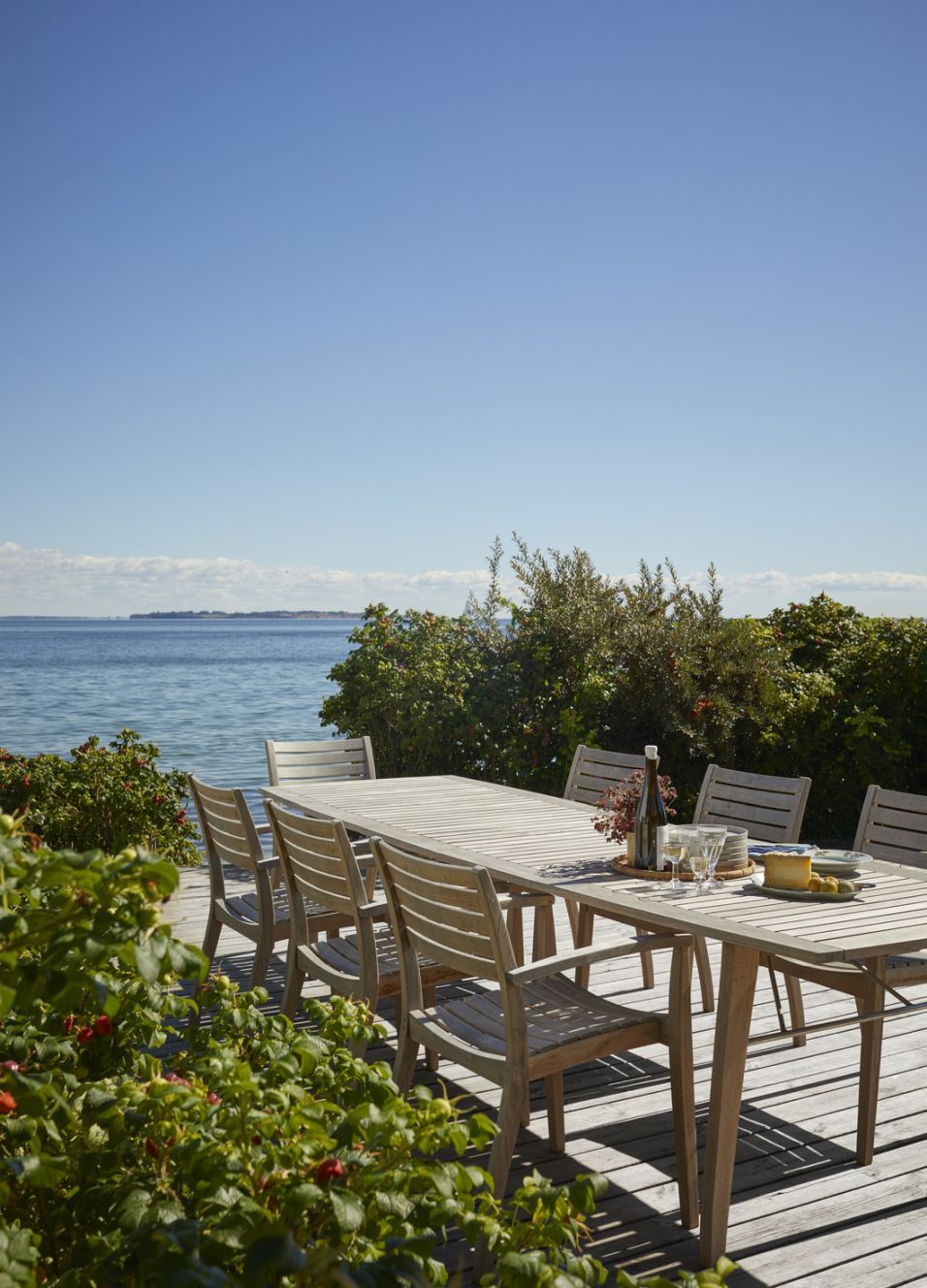 Ballare Table Tisch von Skagerak by Fritz Hansen: Heller Holz-Gartentisch mit Stühlen auf Terrasse am Meer.