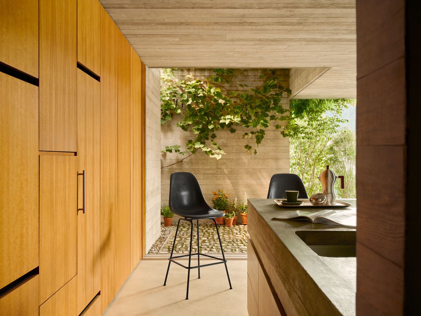 Schwarzer Eames Barhocker von Vitra mit Sitzpolster vor begrünter Betonwand und Holzelementen.