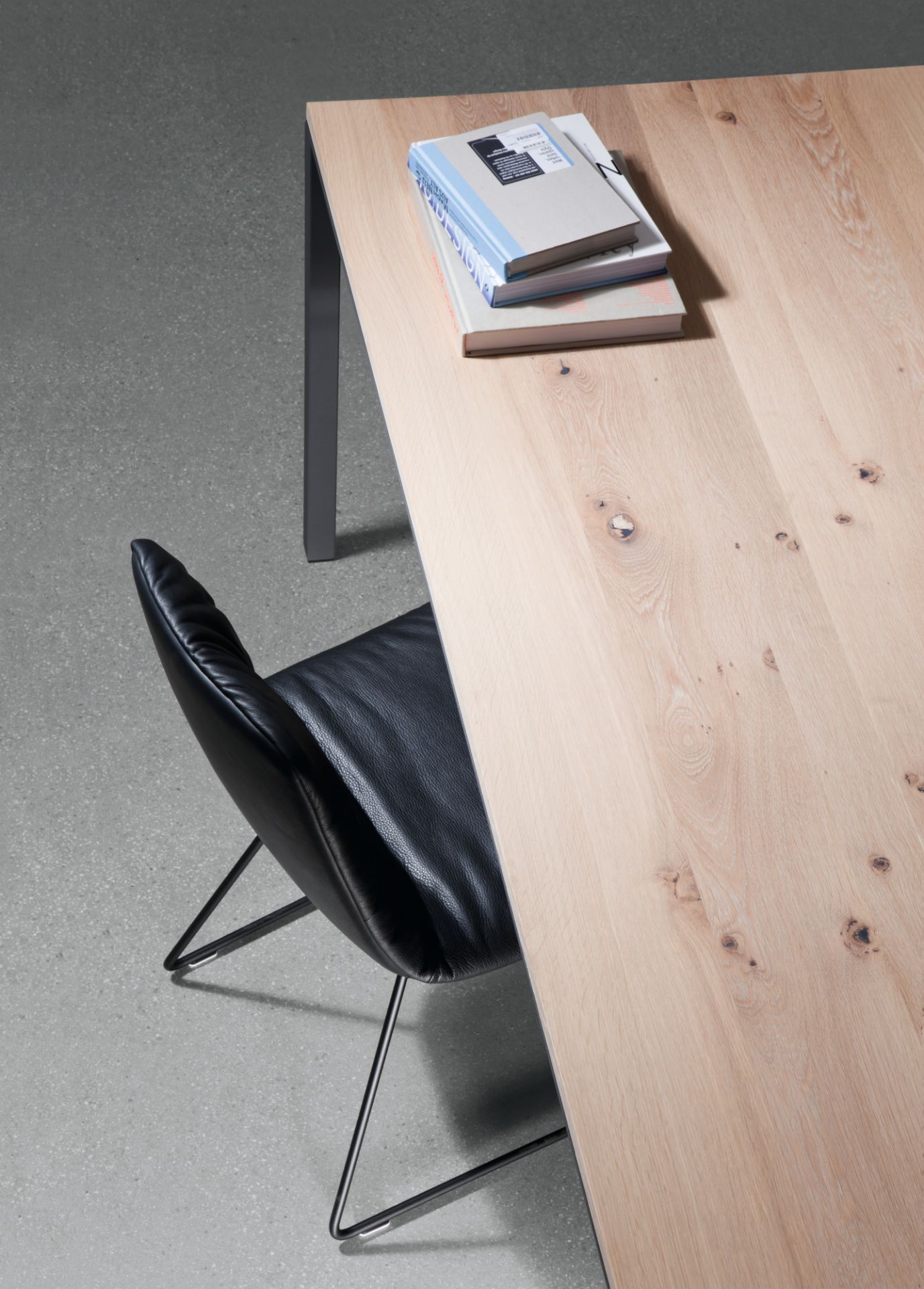 Detailaufnahme Janua S 600 Tisch Eiche mit Bücherstapel und schwarzem Lederstuhl, modernes Möbeldesign für Esszimmer und Büro.
