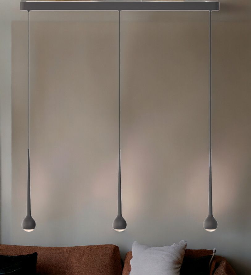 Graue Pendelleuchte im Design "Falling Sun Trace" mit drei Lampen über einem Sofa.