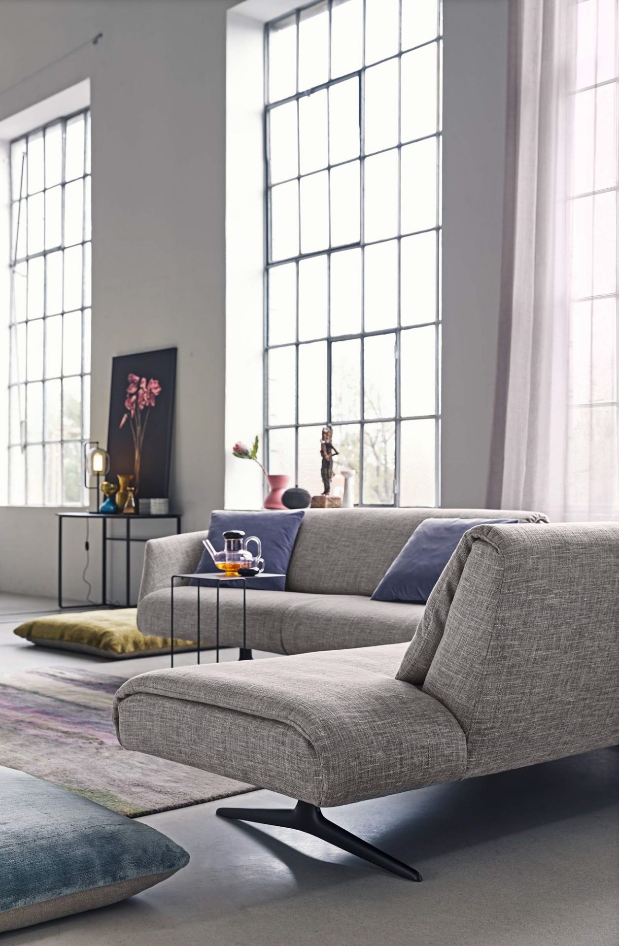Oki Beistelltisch von Walter Knoll neben grauer Couch in modernem Wohnzimmer mit großen Fenstern.