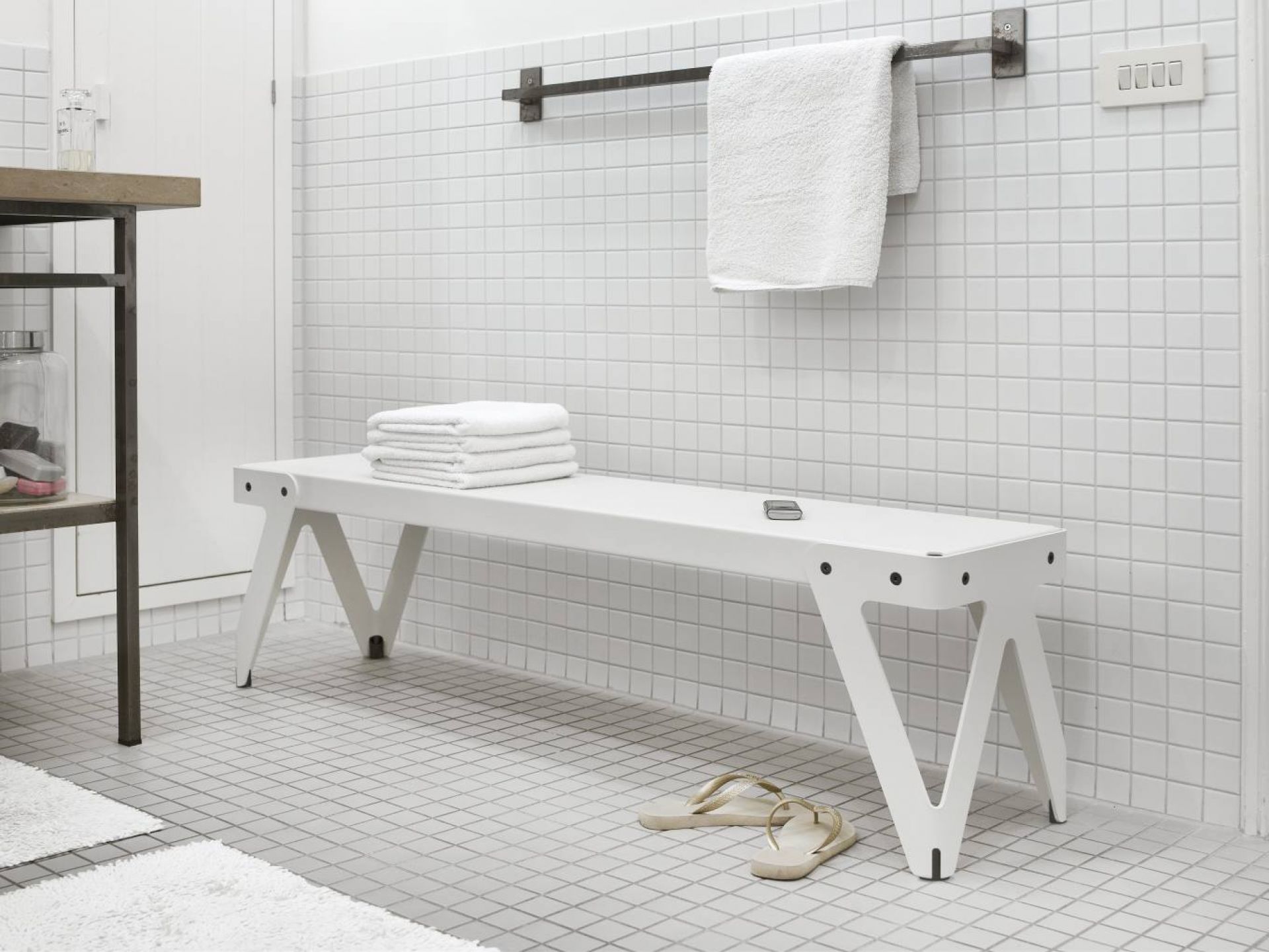 Weißer Lloyd Tisch im Badezimmer mit Handtüchern und Flip-Flops, minimalistisches Design.