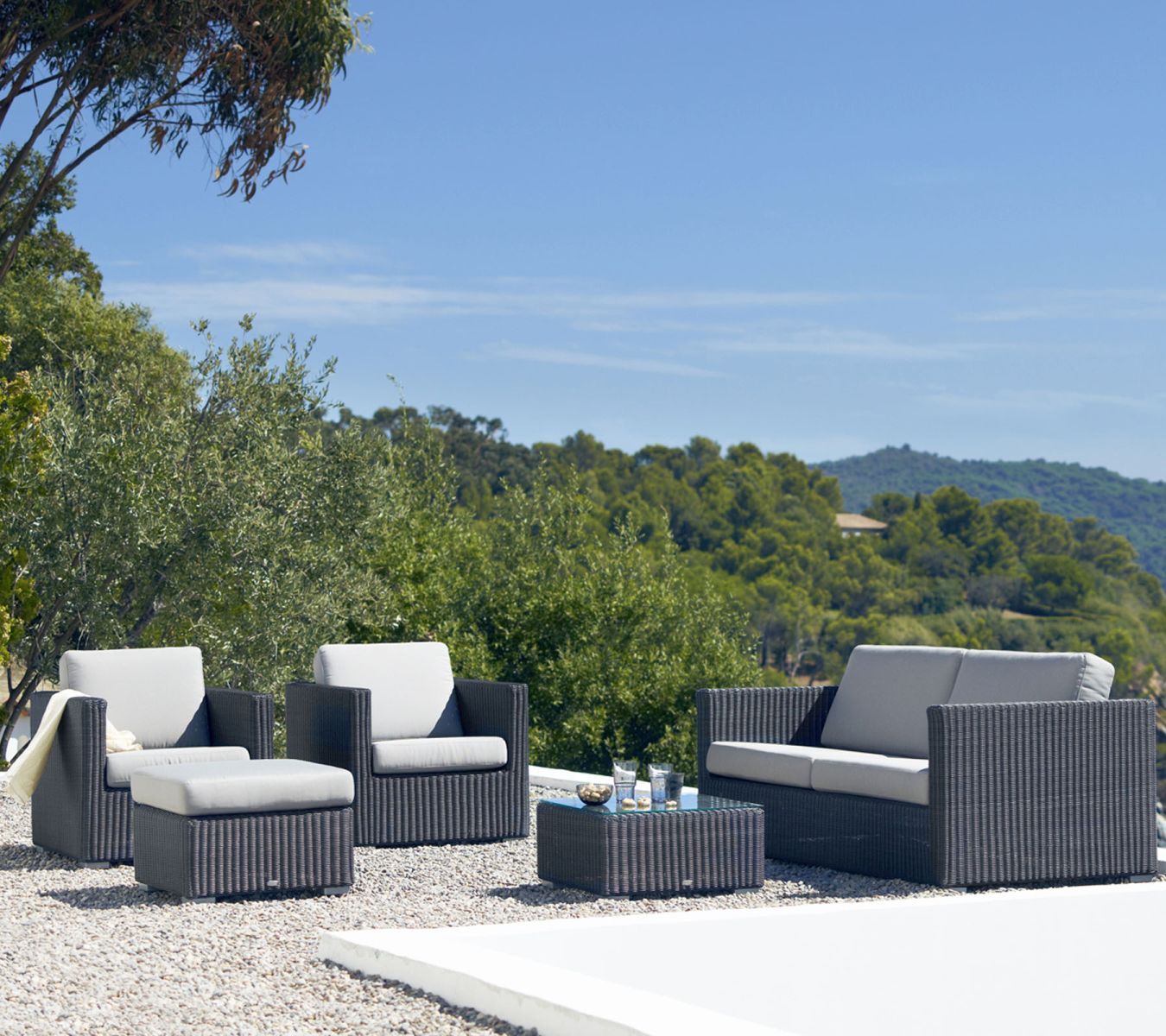 Cane-Line Chester Lounge Möbel: Graphitfarbener Hocker, Sessel, Sofa und Couchtisch im Garten.