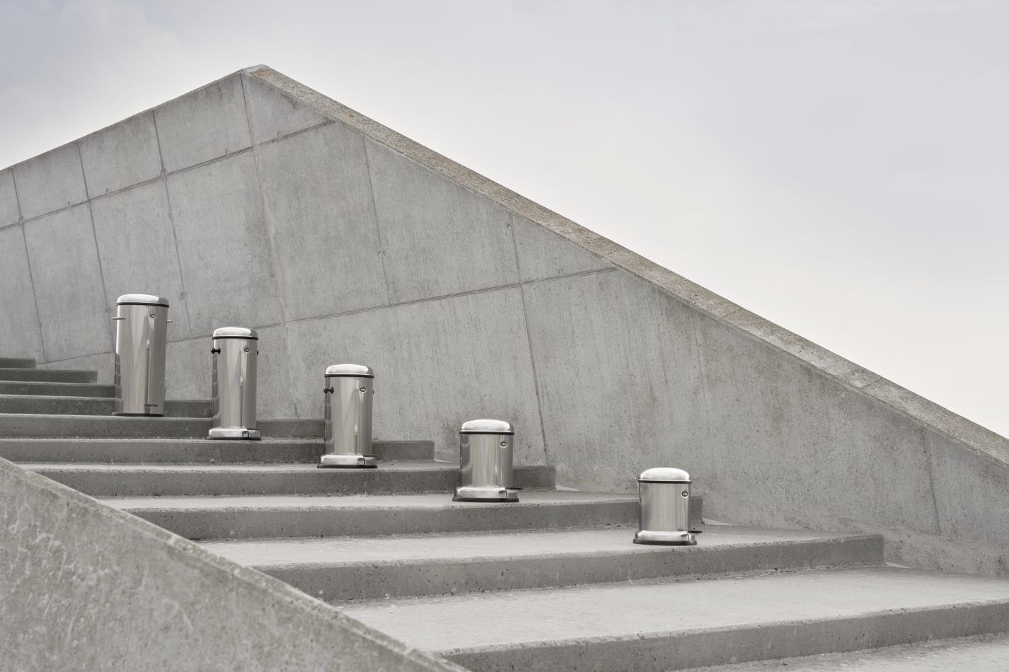 Mehrere Vipp Treteimer aus Edelstahl auf einer Betontreppe vor einer Betonwand.