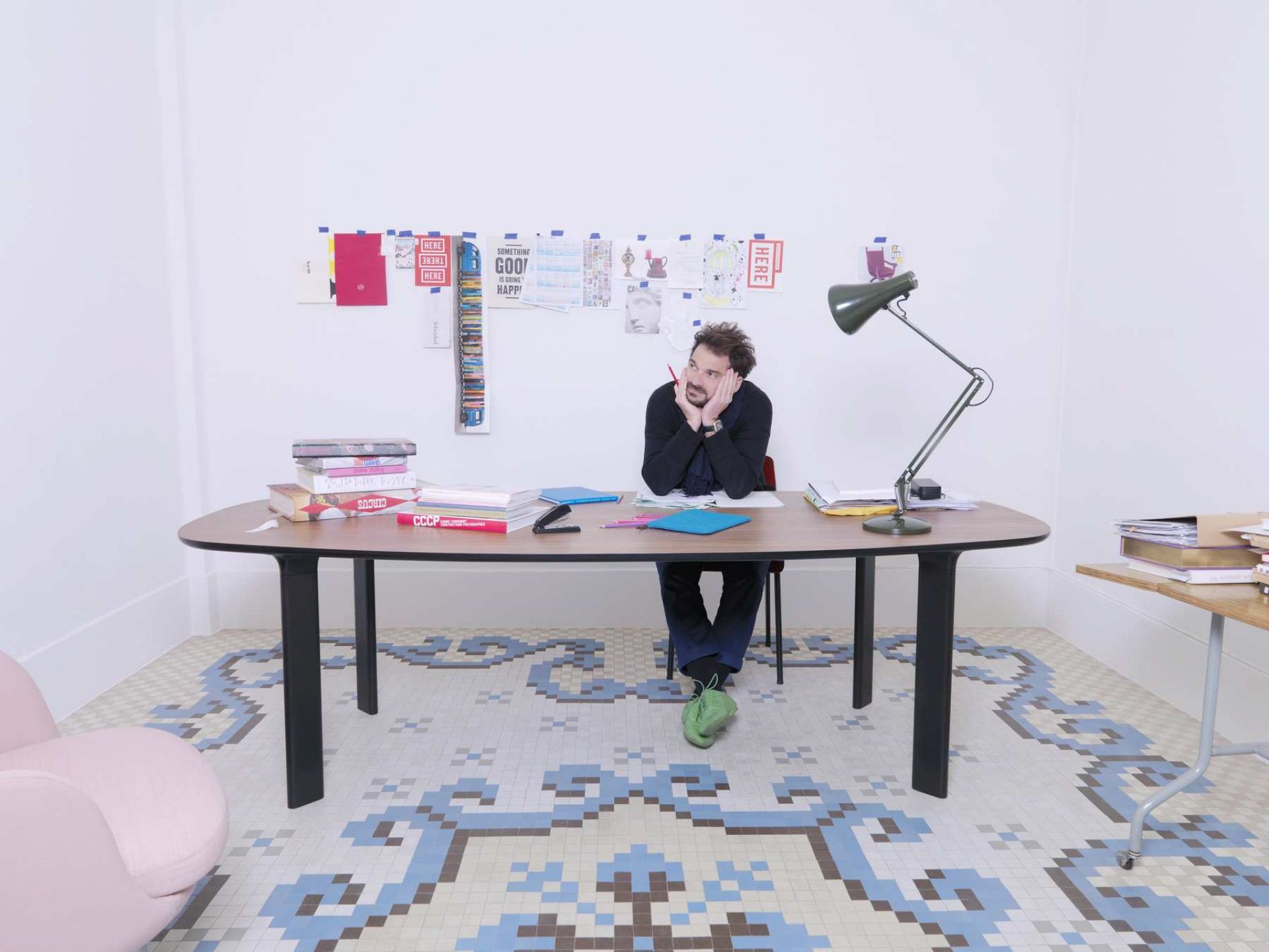 Mann sitzt nachdenklich am Fritz Hansen Analog Tisch mit Büchern und Papieren in einem kreativen Arbeitszimmer.