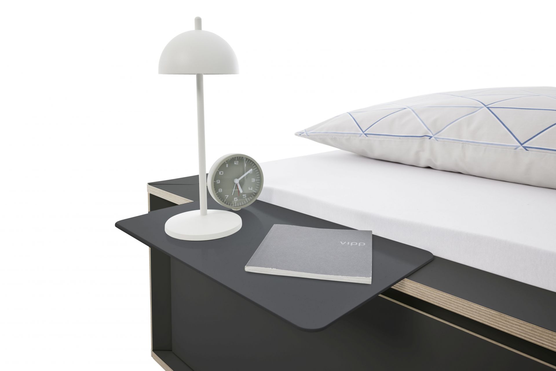 Spaze Bett von Müller Möbelwerkstätten mit Nachttisch, Lampe, Uhr und Kissen im Schlafzimmer.