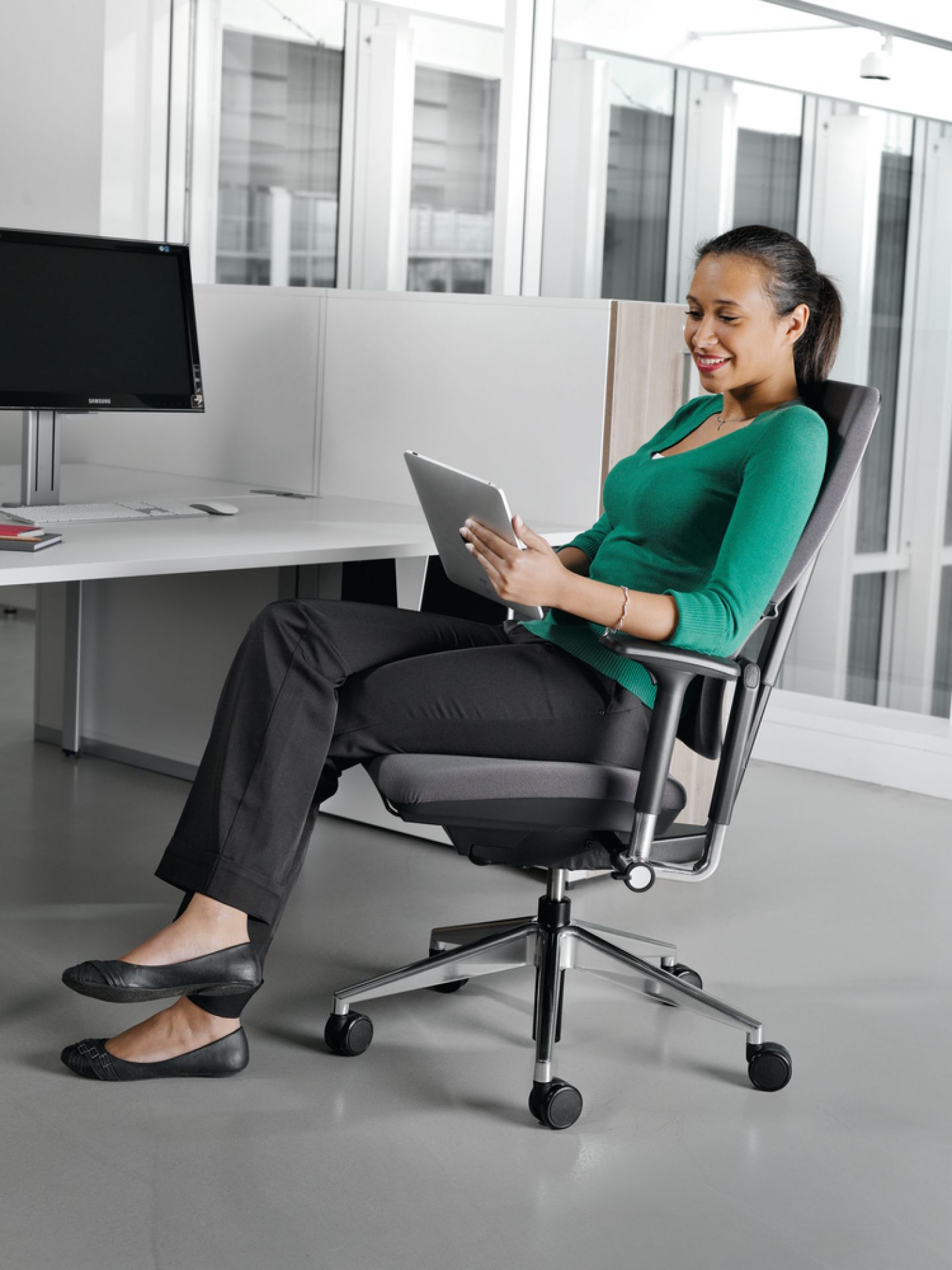 Frau sitzt entspannt auf einem grauen Steelcase Please Drehstuhl und nutzt ein Tablet.