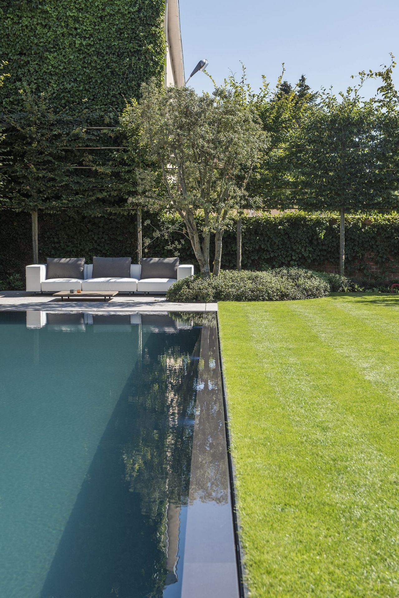 Walrus Outdoor Eckmodul Sofa von Extremis neben einem Pool in einem gepflegten Garten.