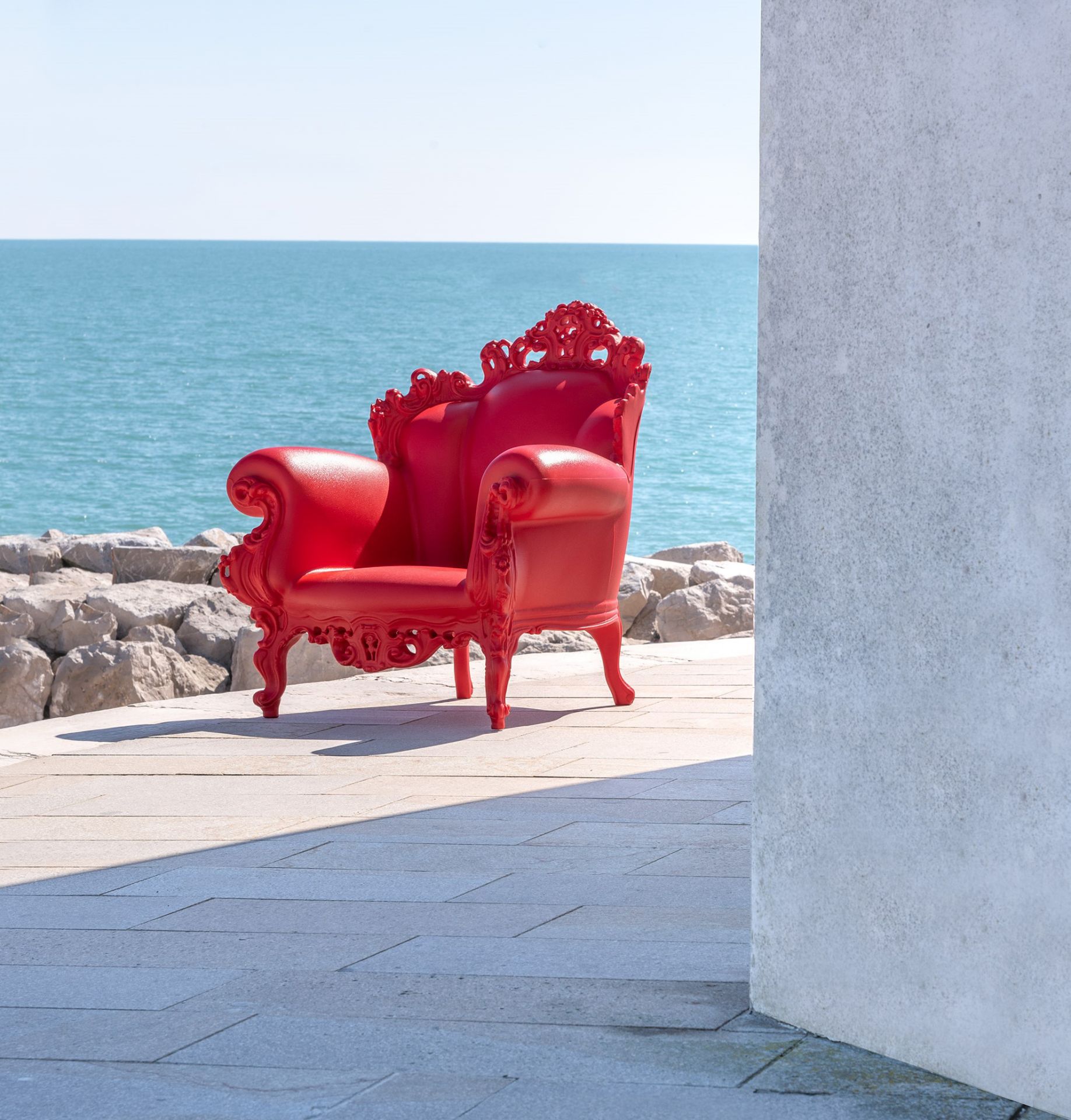 Roter Magis Proust Sessel für den Außenbereich vor blauem Meer und Felsen.
