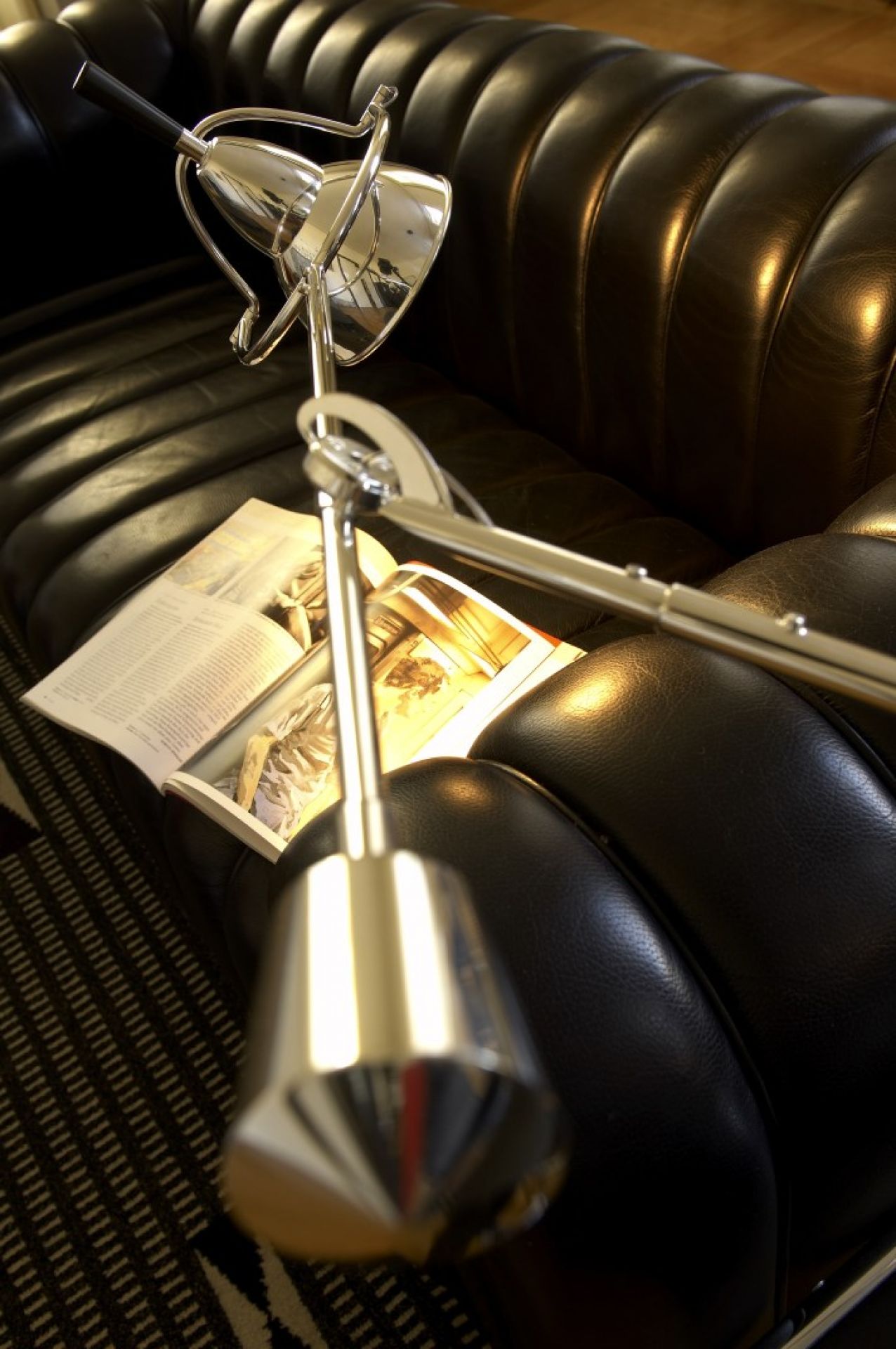 Moderne, verstellbare Chrom-Stehlampe auf einer schwarzen Ledercouch mit Zeitschrift für gemütliches Wohnambiente.