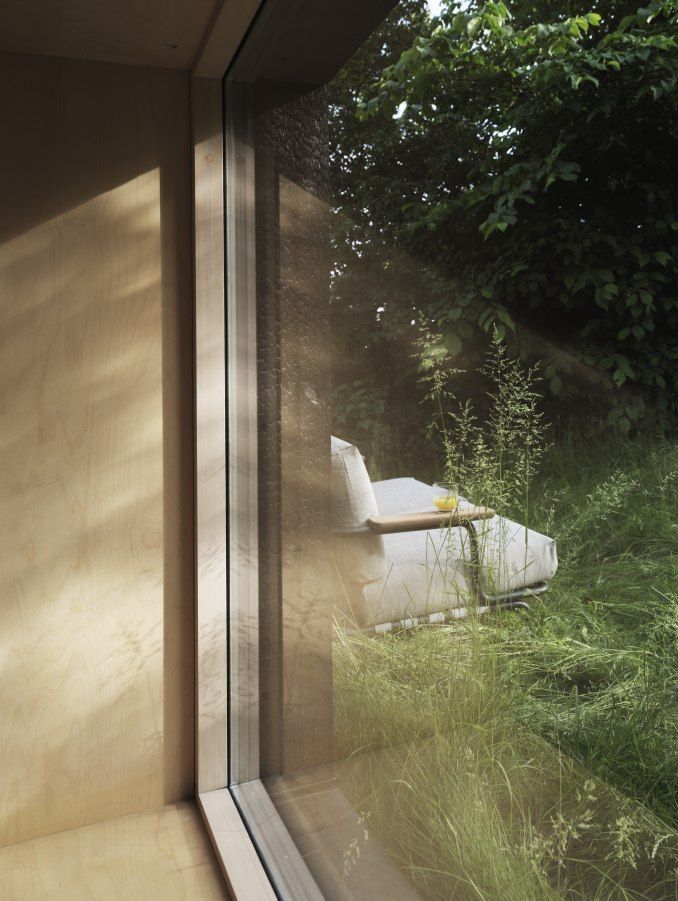 Settle Outdoor Sofa von Muuto, ein bequemes 2-Sitzer Gartensofa im Grünen, gesehen durch ein Fenster.