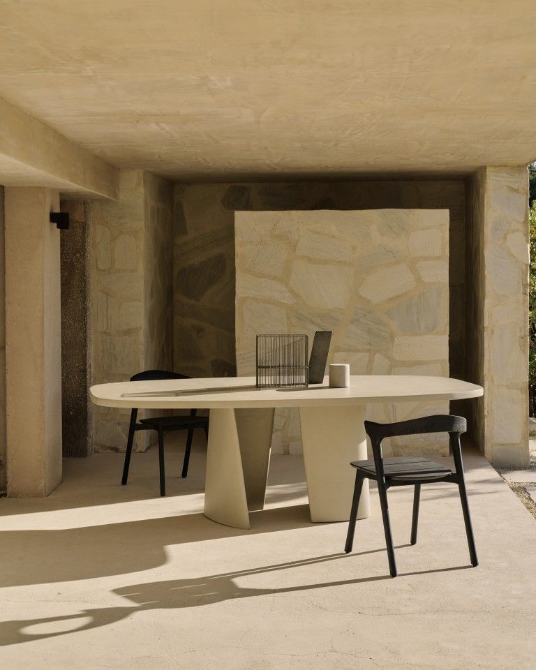 Canyon Outdoor Esstisch von Ethnicraft, oval, aus Beton mit zwei schwarzen Stühlen auf Terrasse.