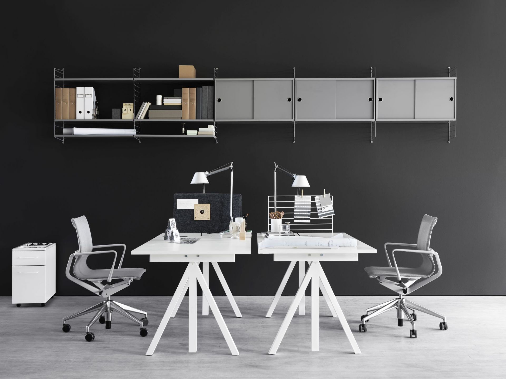 Zwei weiße Schreibtische mit String Regalsystem an schwarzer Wand. Büro, Arbeitsplatz, Homeoffice.
